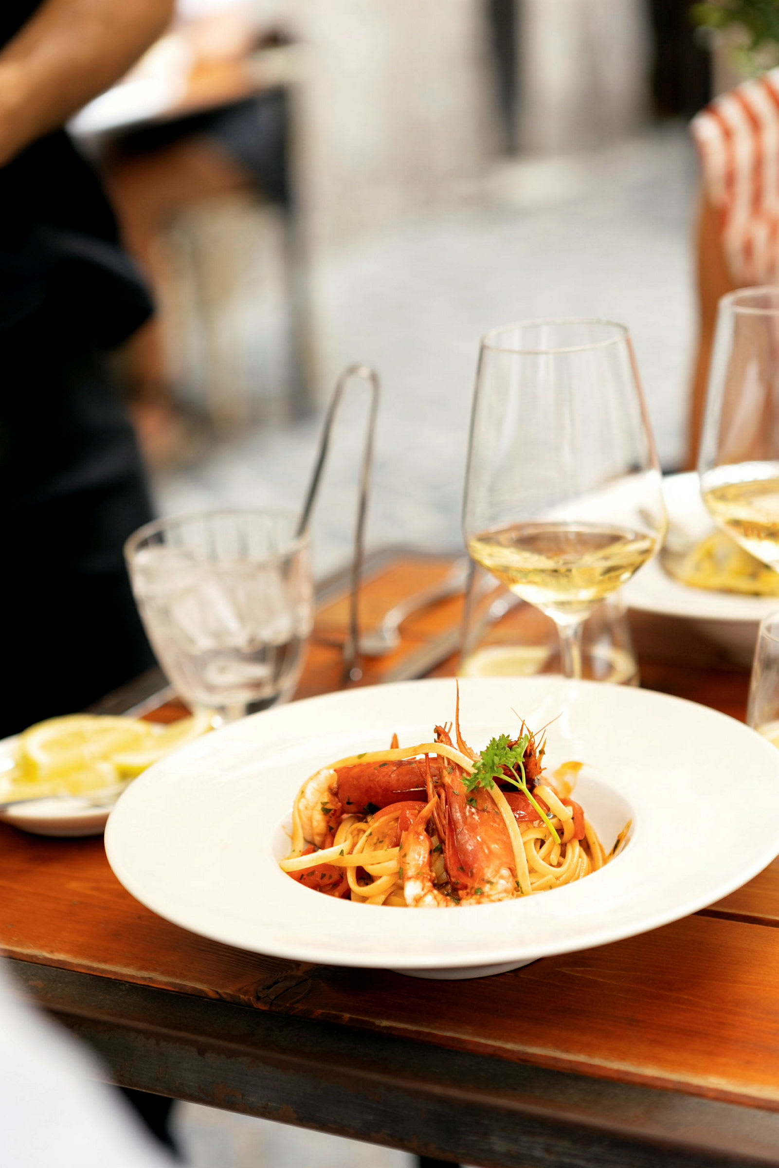 En tallerken med pasta og sjømat på et trebord, omgitt av glass og bestikk. (AI-generert tekst)