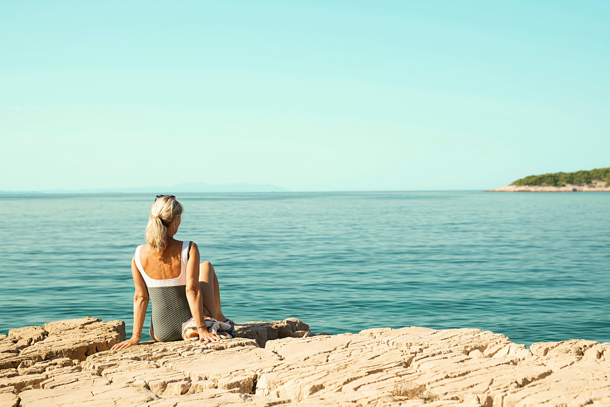En person sitter på en steinete kyst og ser utover havet. (AI-generert tekst)