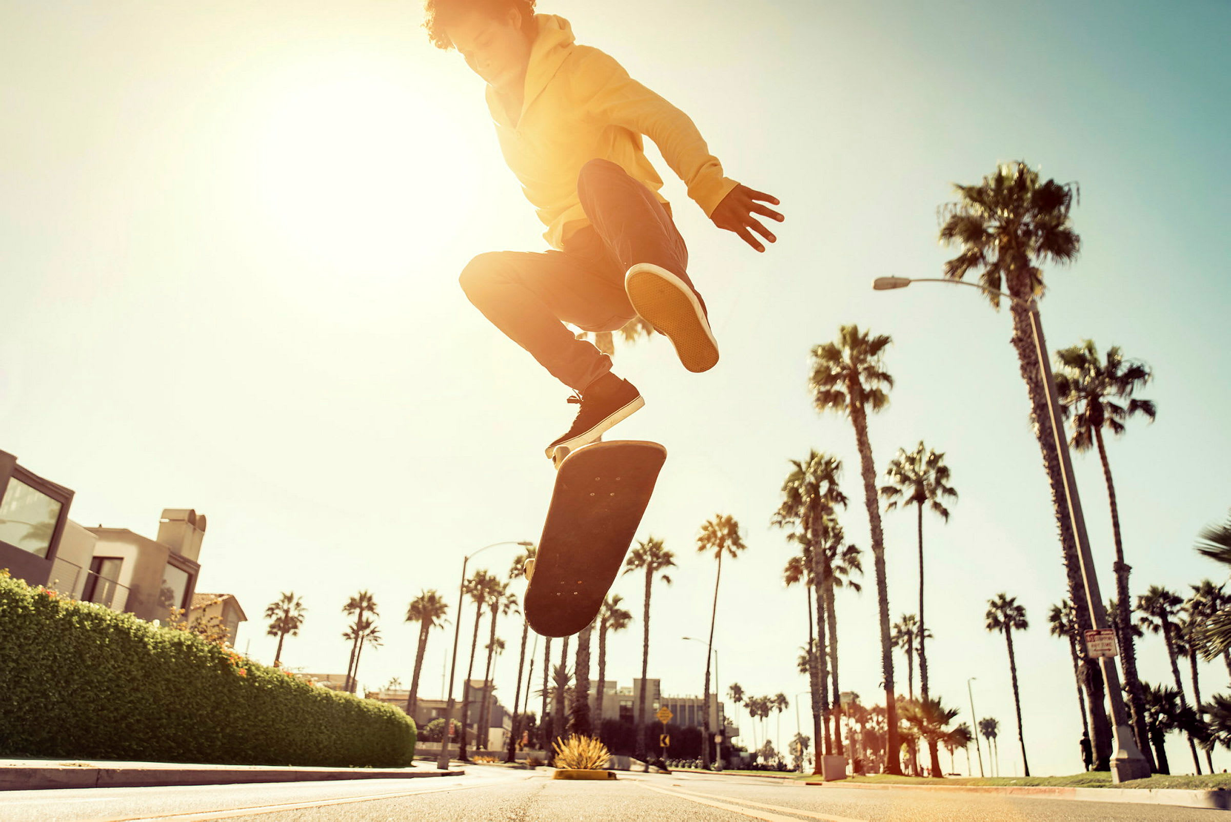 En person utfører et skateboardtriks på en gate omgitt av palmetrær ved solnedgang. (AI-generert tekst)