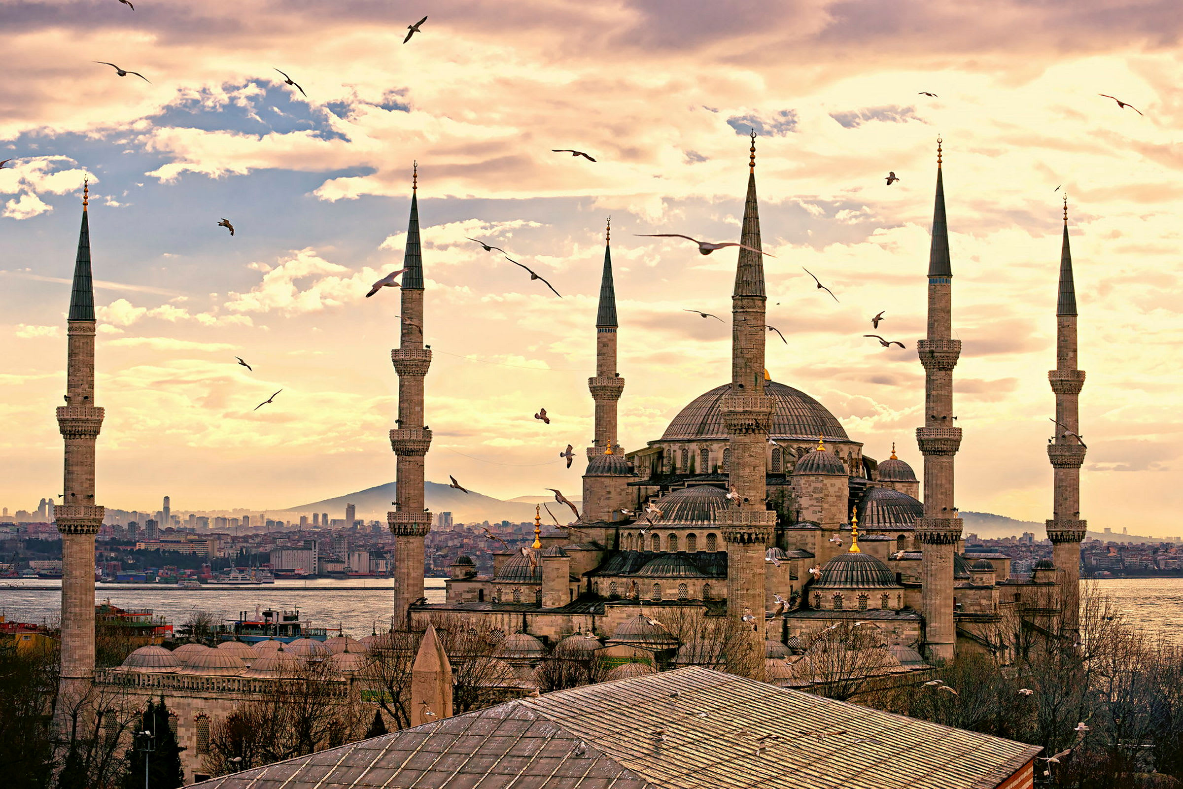 Bilde av en stor moské med høye minareter og omkringliggende arkitektur med en bakgrunn av himmel og by. (AI-generert tekst)