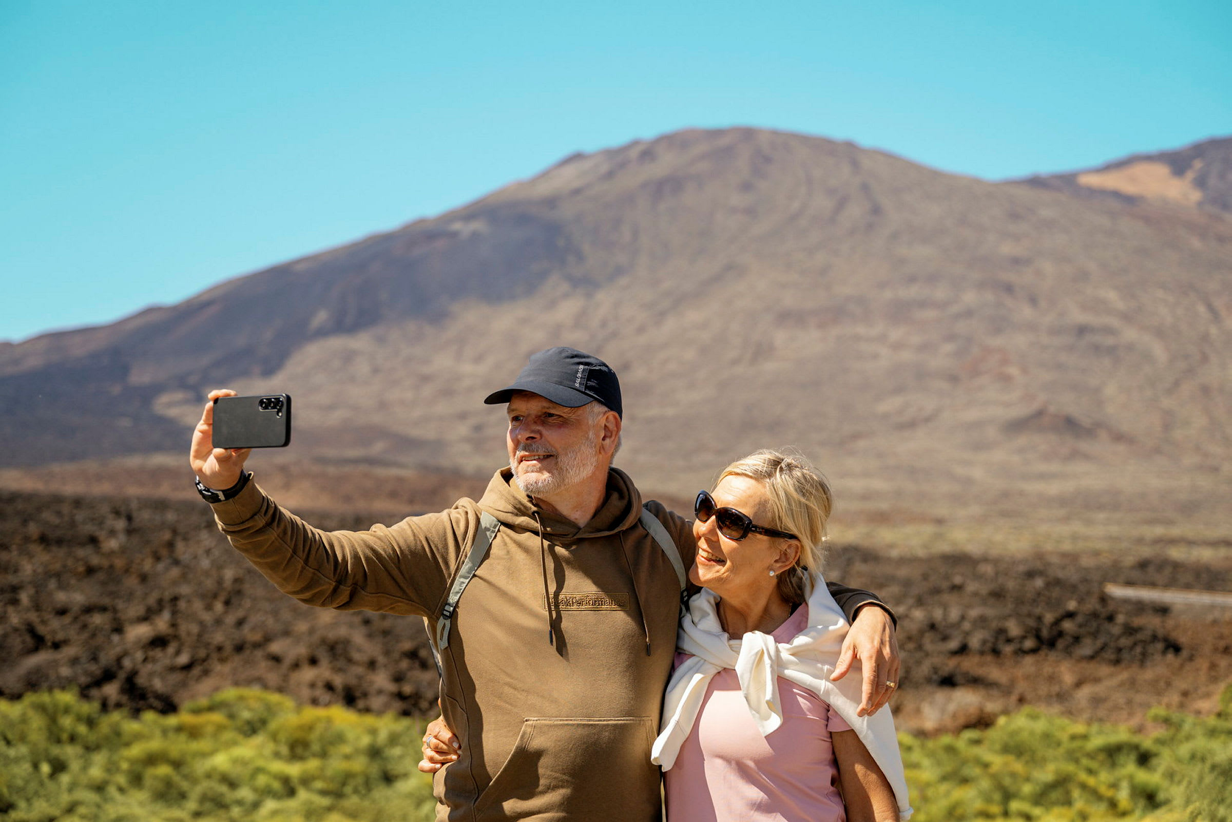 To personer tar en selfie foran et fjell i solfylt vær. (AI-generert tekst)