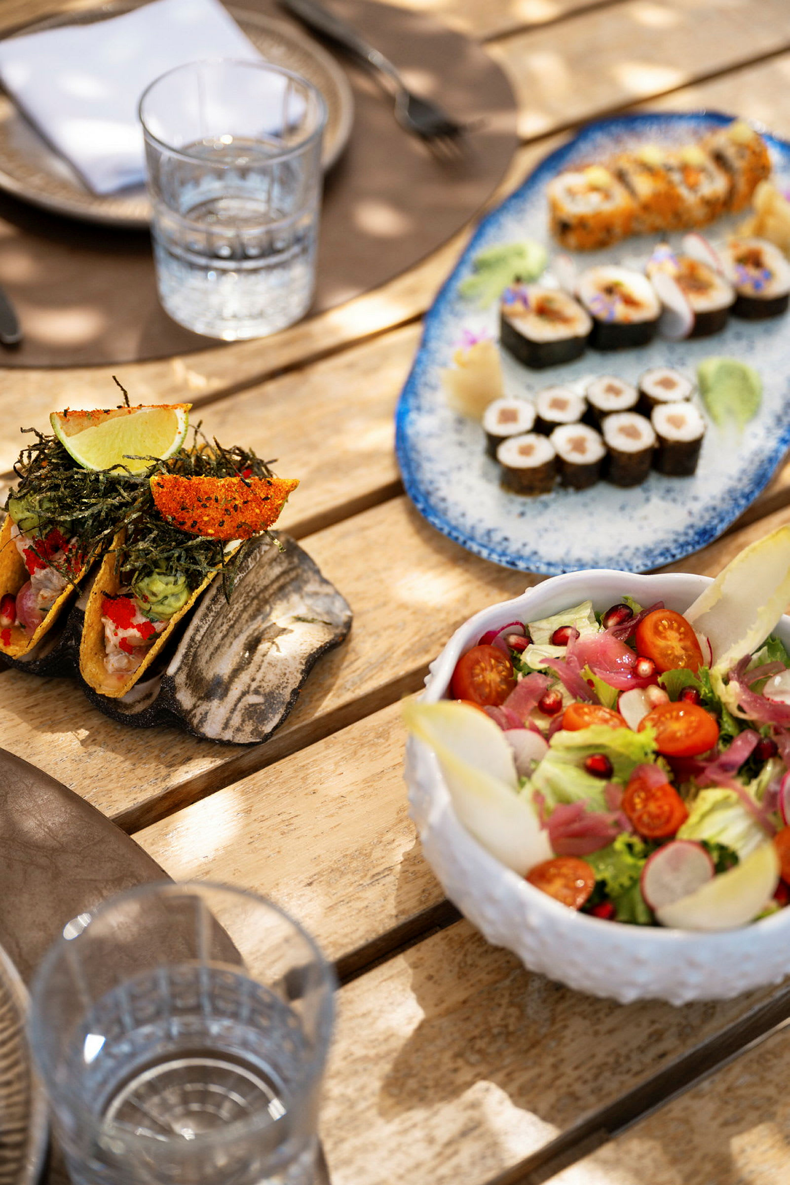Borddekking med salat, sushi og små tacos. (AI-generert tekst)