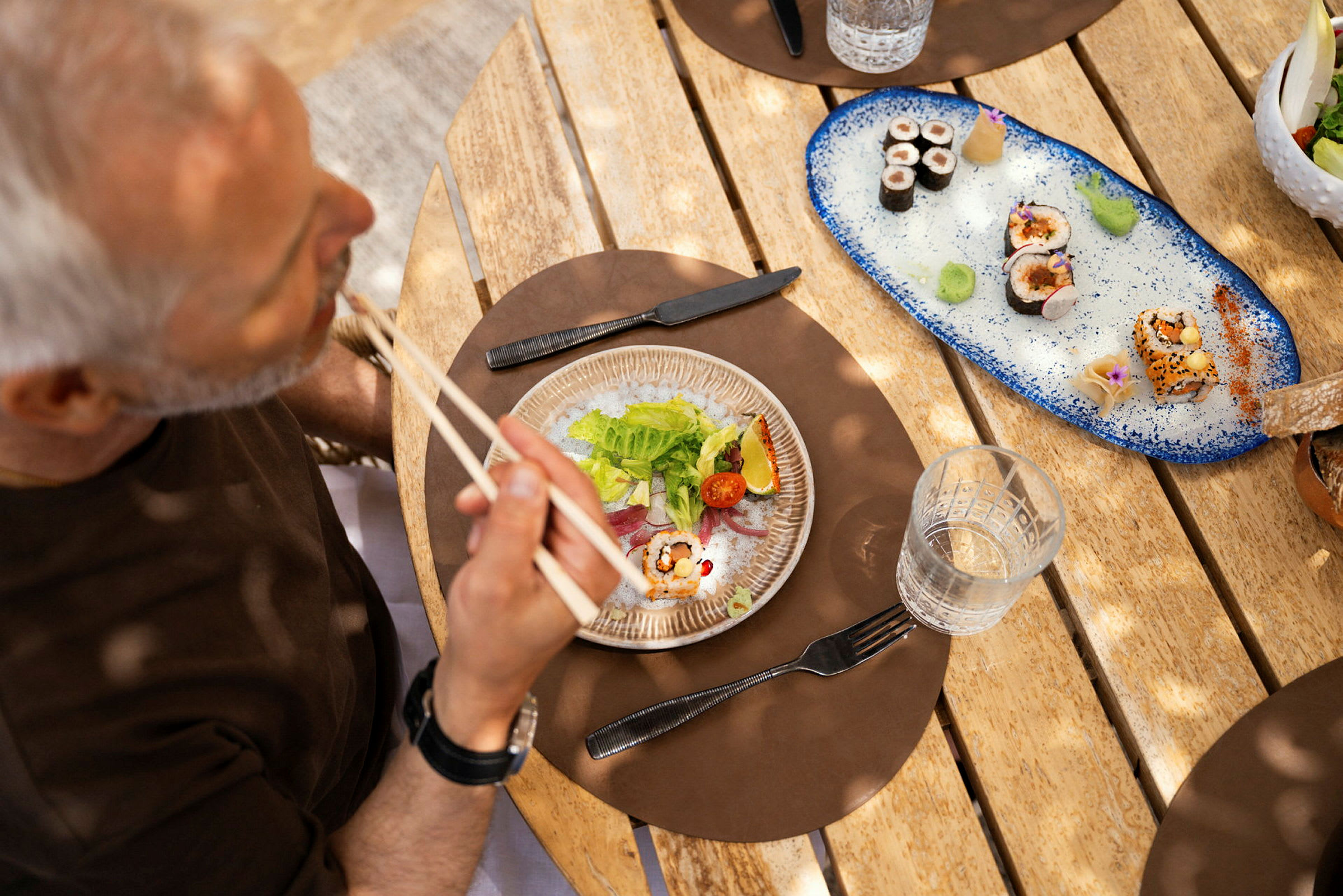 En person spiser sushi ved et trebord. (AI-generert tekst)