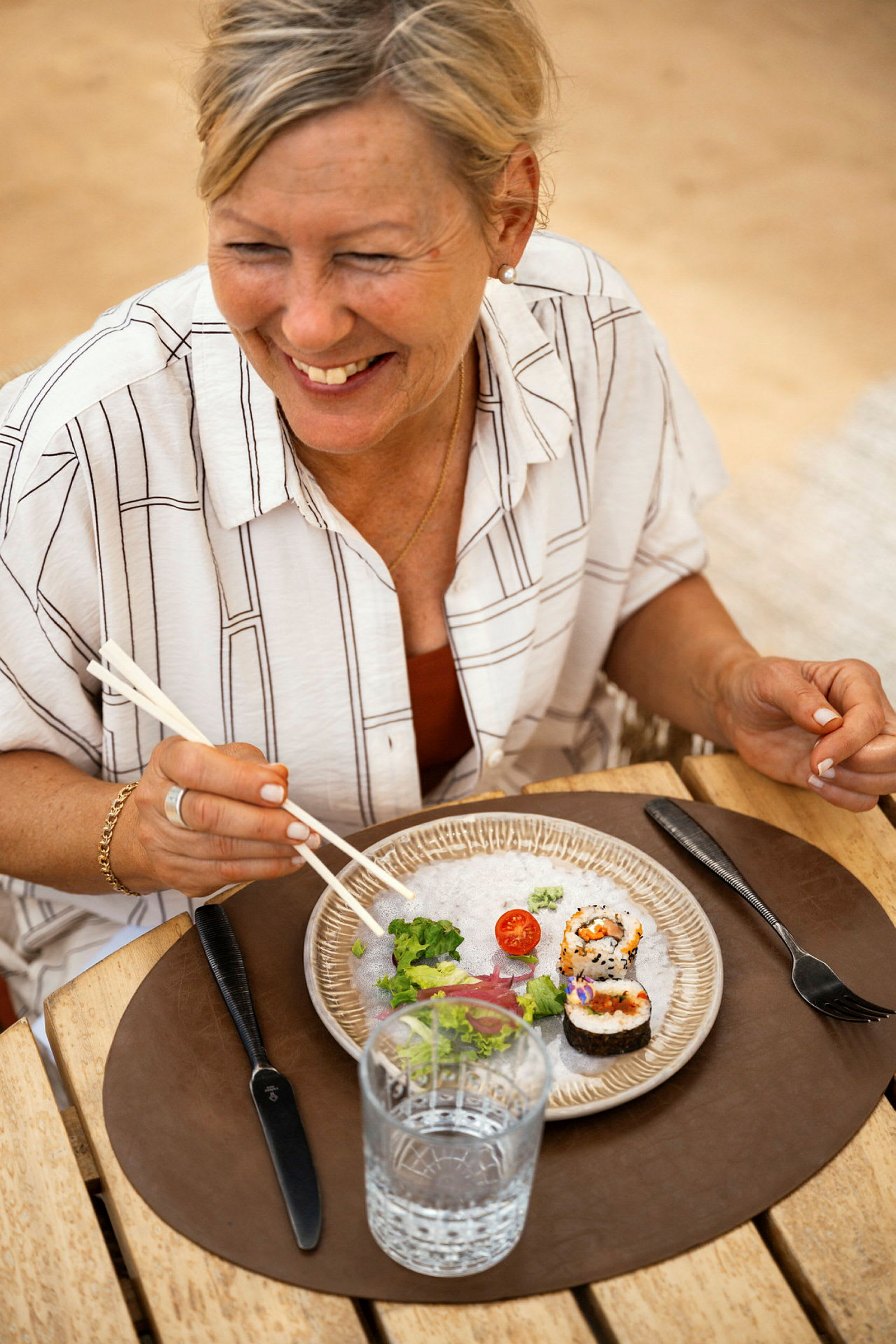 En person spiser sushi ved et bord, med en tallerken og et glass vann foran seg. (AI-generert tekst)