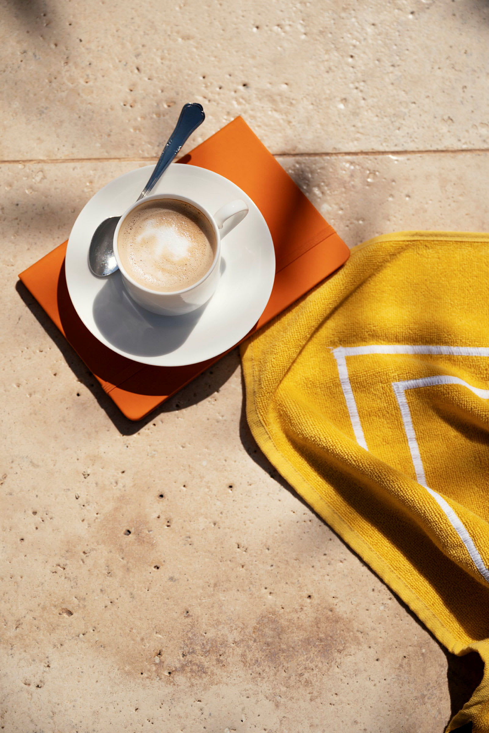 En kopp kaffe med en skje er på en tallerken med en oransje bok og et gult håndkle. (AI-generert tekst)