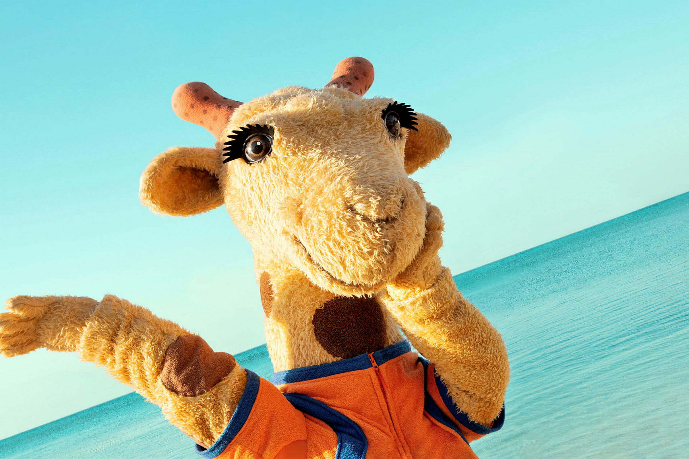 Maskotten giraff ved stranden. (AI-generert tekst)