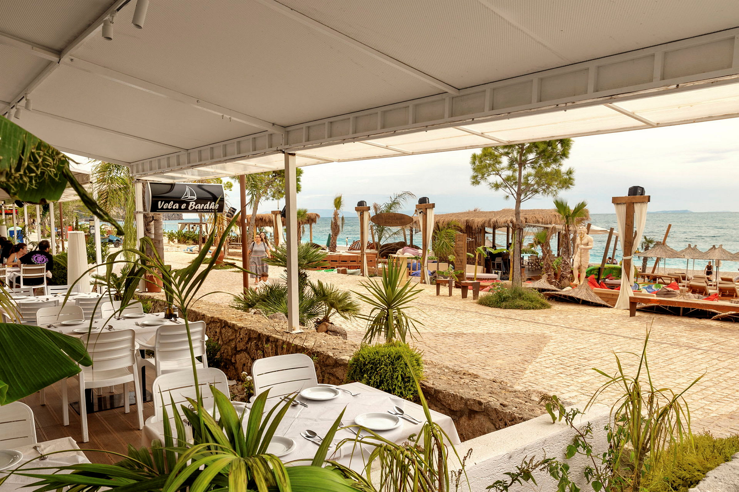 Strandnær restaurant med hvite bord og stoler, havutsikt og solsenger. (AI-generert tekst)