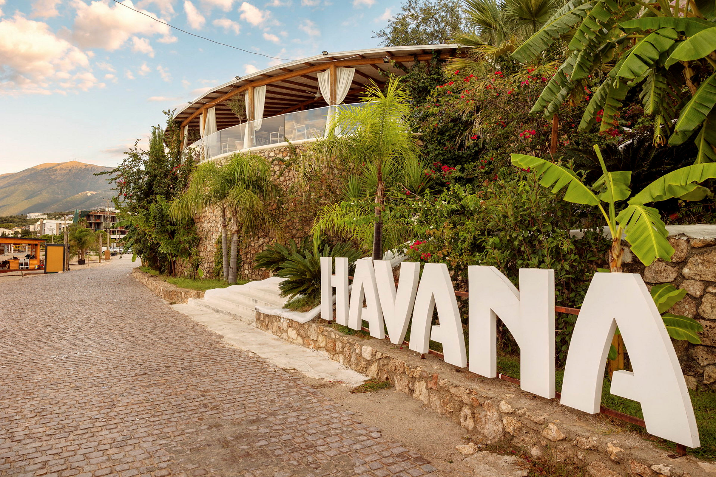 Skrevet tekst med 'HAVANA' ved en tropisk bygning ved siden av brosteinsvei. (AI-generert tekst)