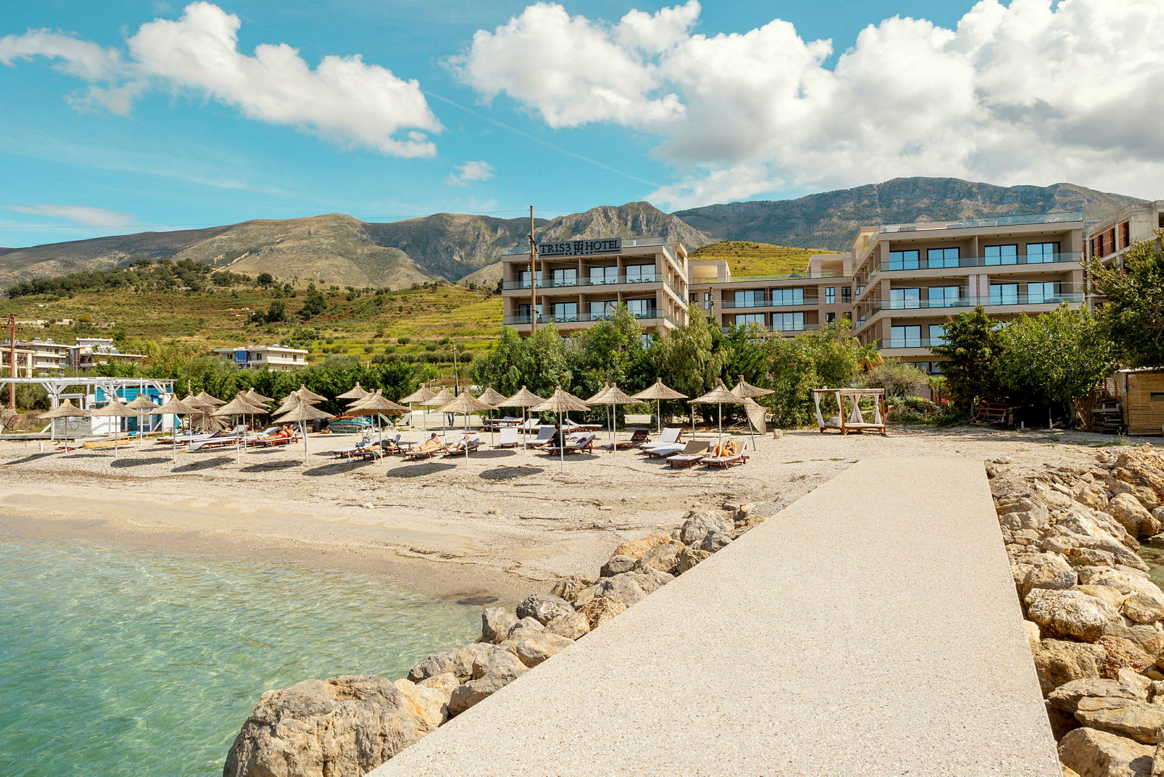 Hotelutsikt ved en steinete strand med parasoller og solsenger. (AI-generert tekst)