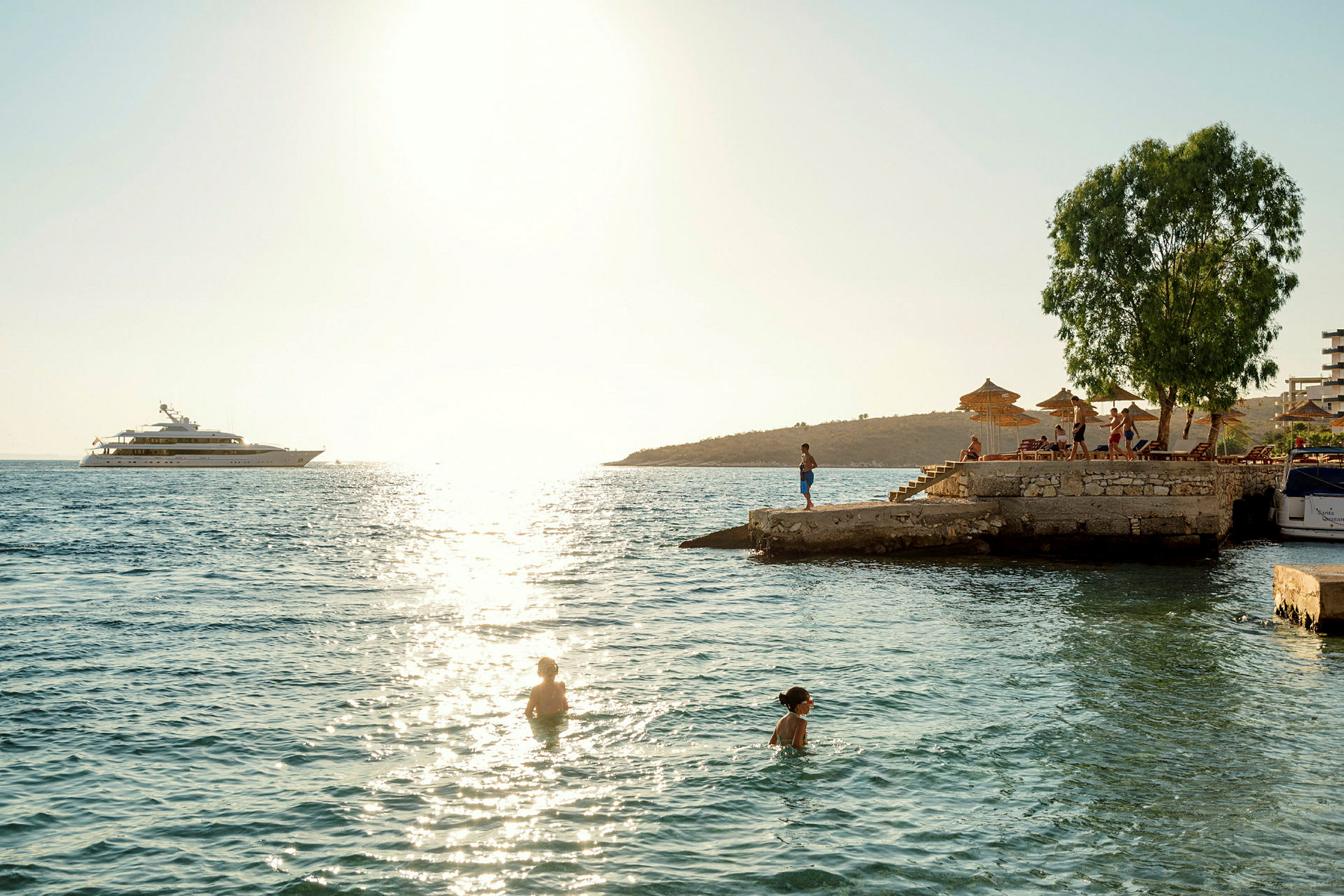 Folk svømmer i havet nær en brygge med solsenger og parasoller. (AI-generert tekst)