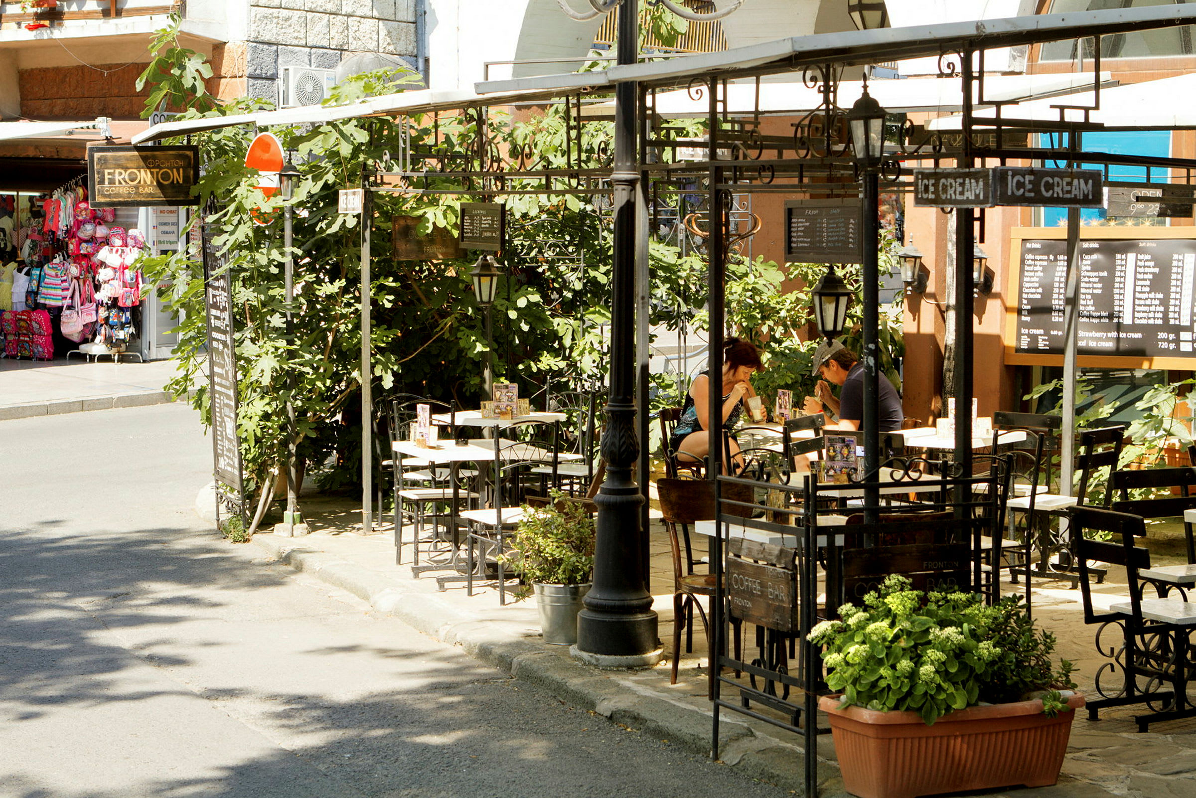 Utendørs kafé med planter, bord og meny skilt. (AI-generert tekst)