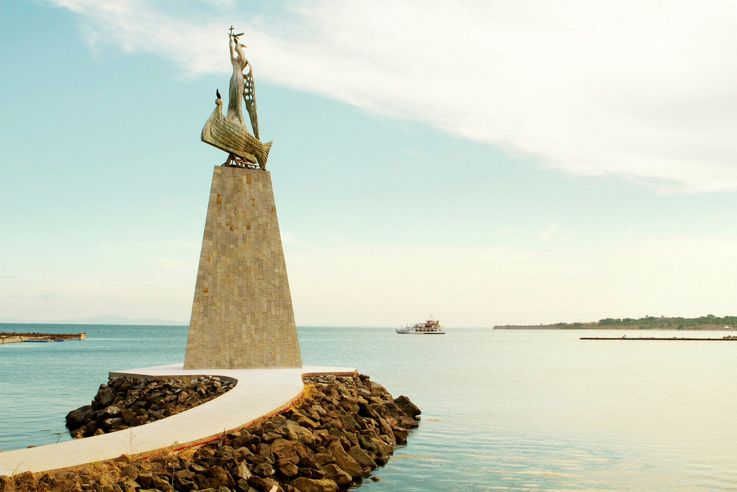 Et monument med en skulptur av et skip, plassert ved en brygge omgitt av vann. (AI-generert tekst)