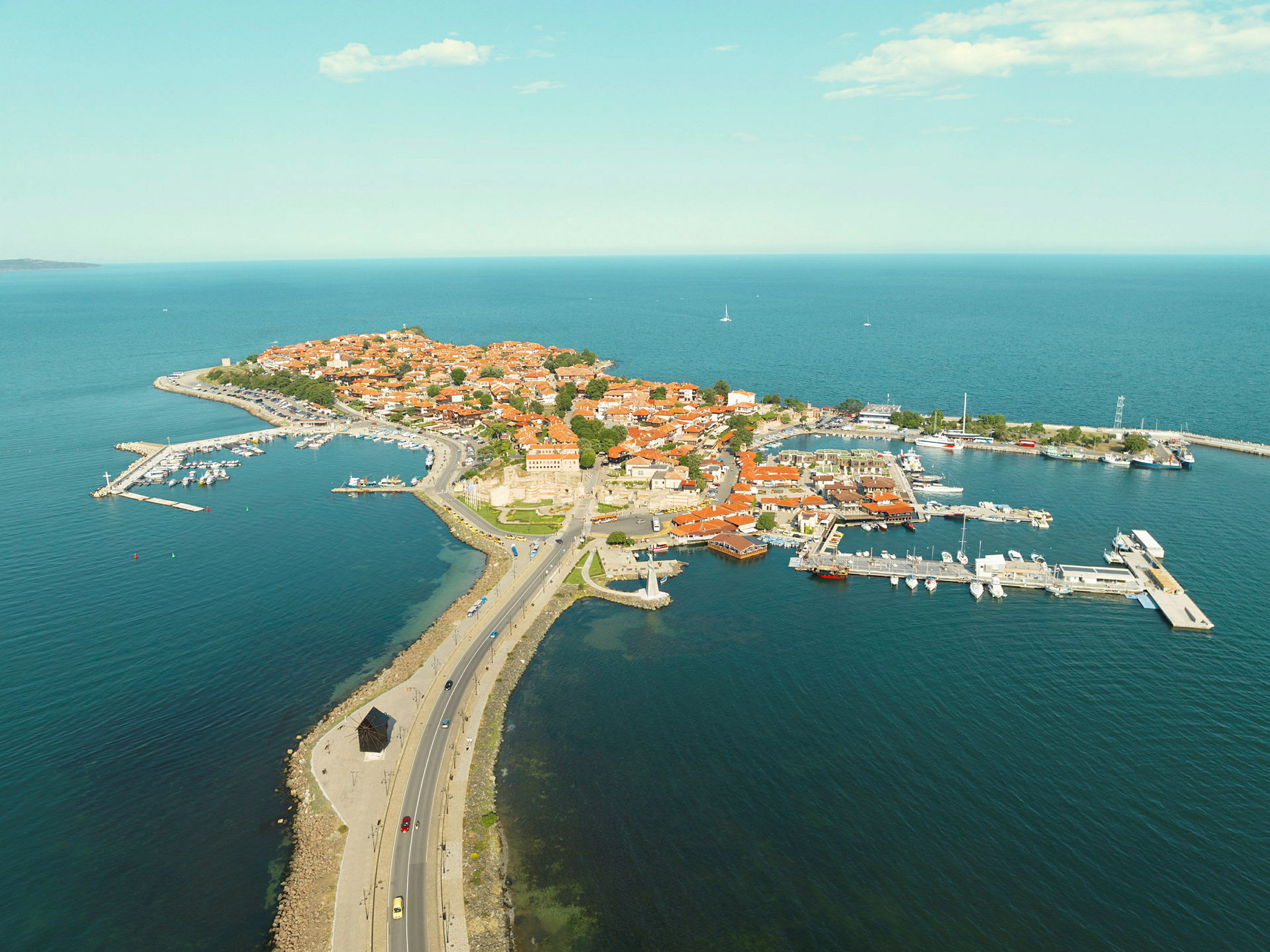 Luftfoto av en halvøy med røde tak og havn. (AI-generert tekst)