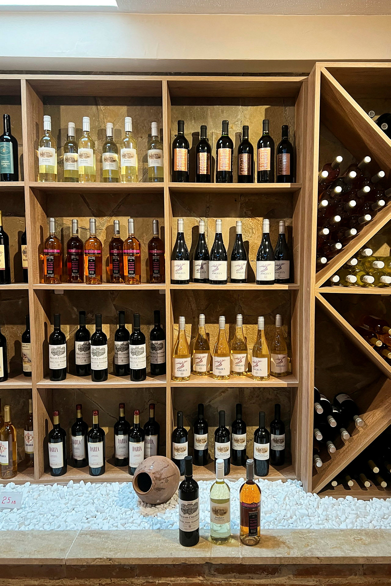 En vegg med hyller fylt med flasker med vin i forskjellige farger og typer. (AI-generert tekst)