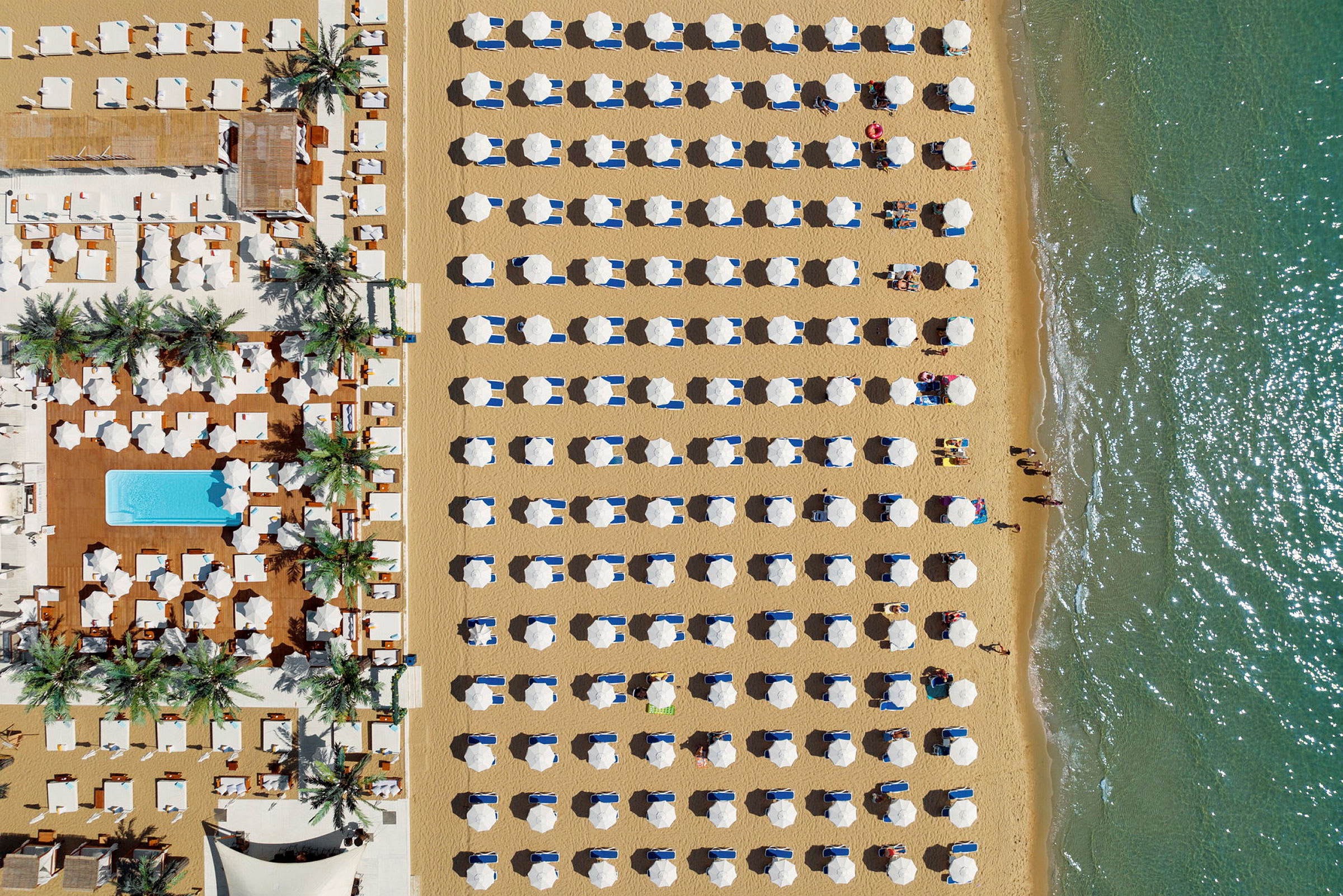 Luftfoto av en strand med organiserte parasoller og solstoler nær vannet. (AI-generert tekst)