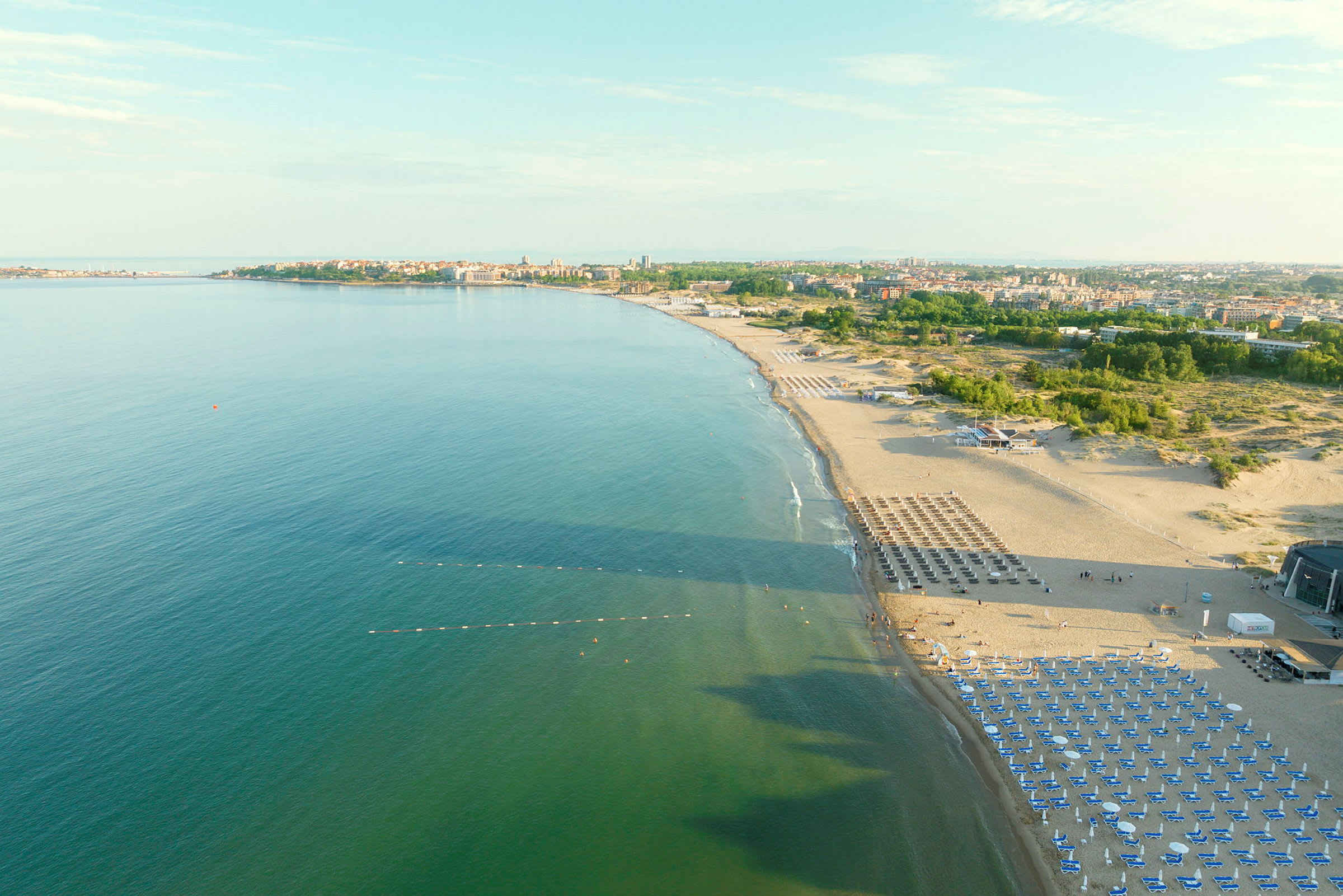 Lang strand med parasoller og solsenger langs klart vann. (AI-generert tekst)