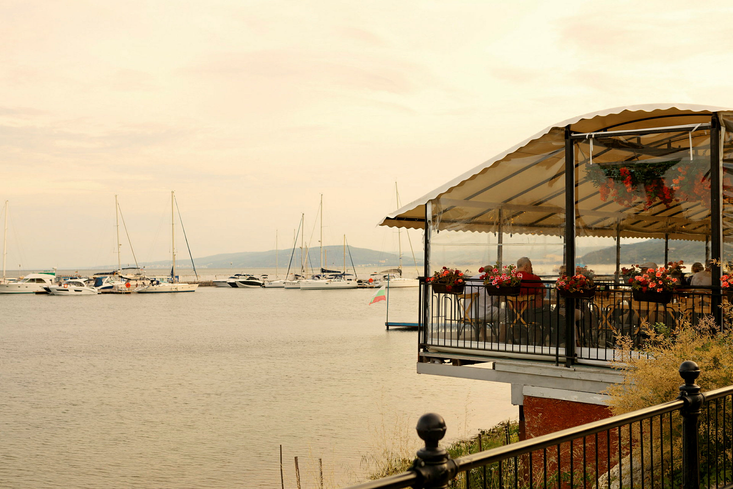 Restaurant med terrasse ved vannet og båter i bakgrunnen. (AI-generert tekst)