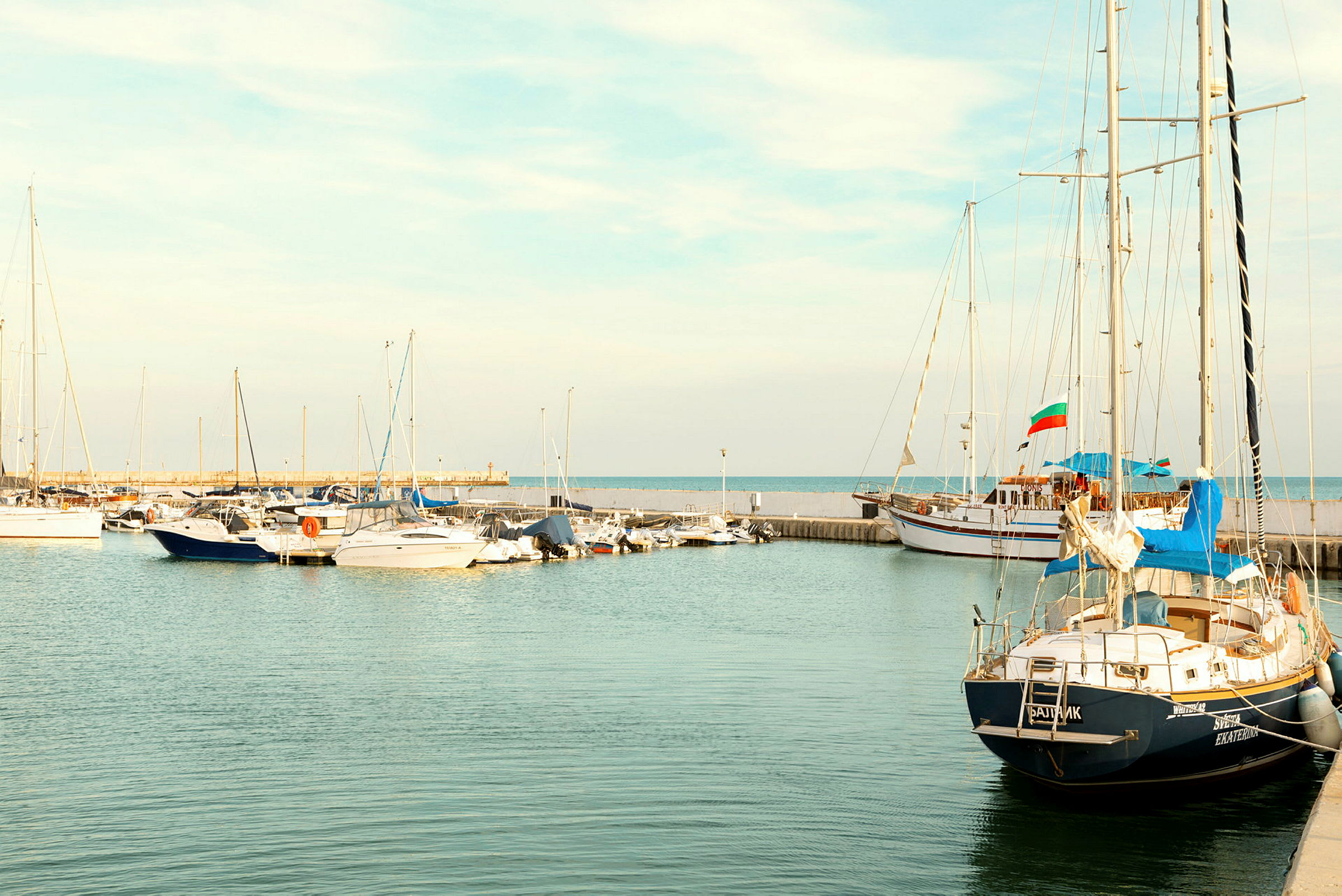 Småbåter og seilfartøy fortøyd i havnen, med havet i bakgrunnen. (AI-generert tekst)