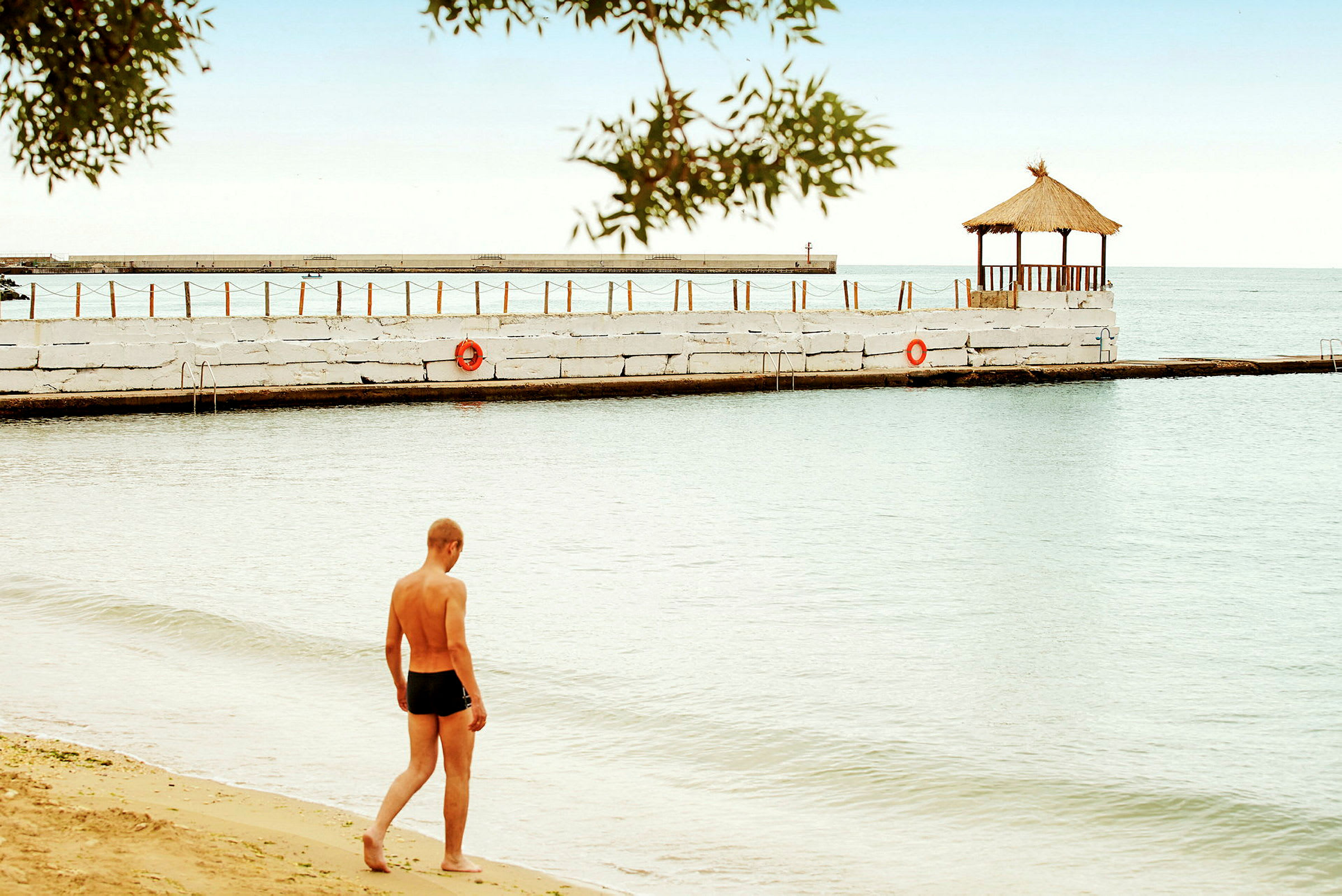 En person spaserer på en strand ved vannet. En paviljong står på en brygge. (AI-generert tekst)