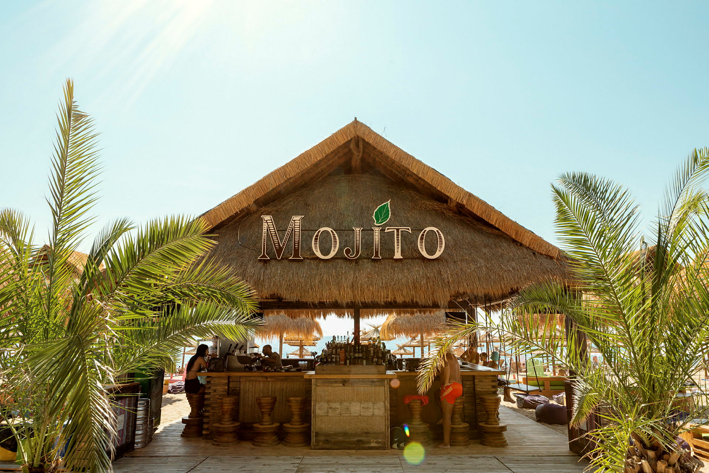En strandbar med stråtak og navnet Mojito. (AI-generert tekst)