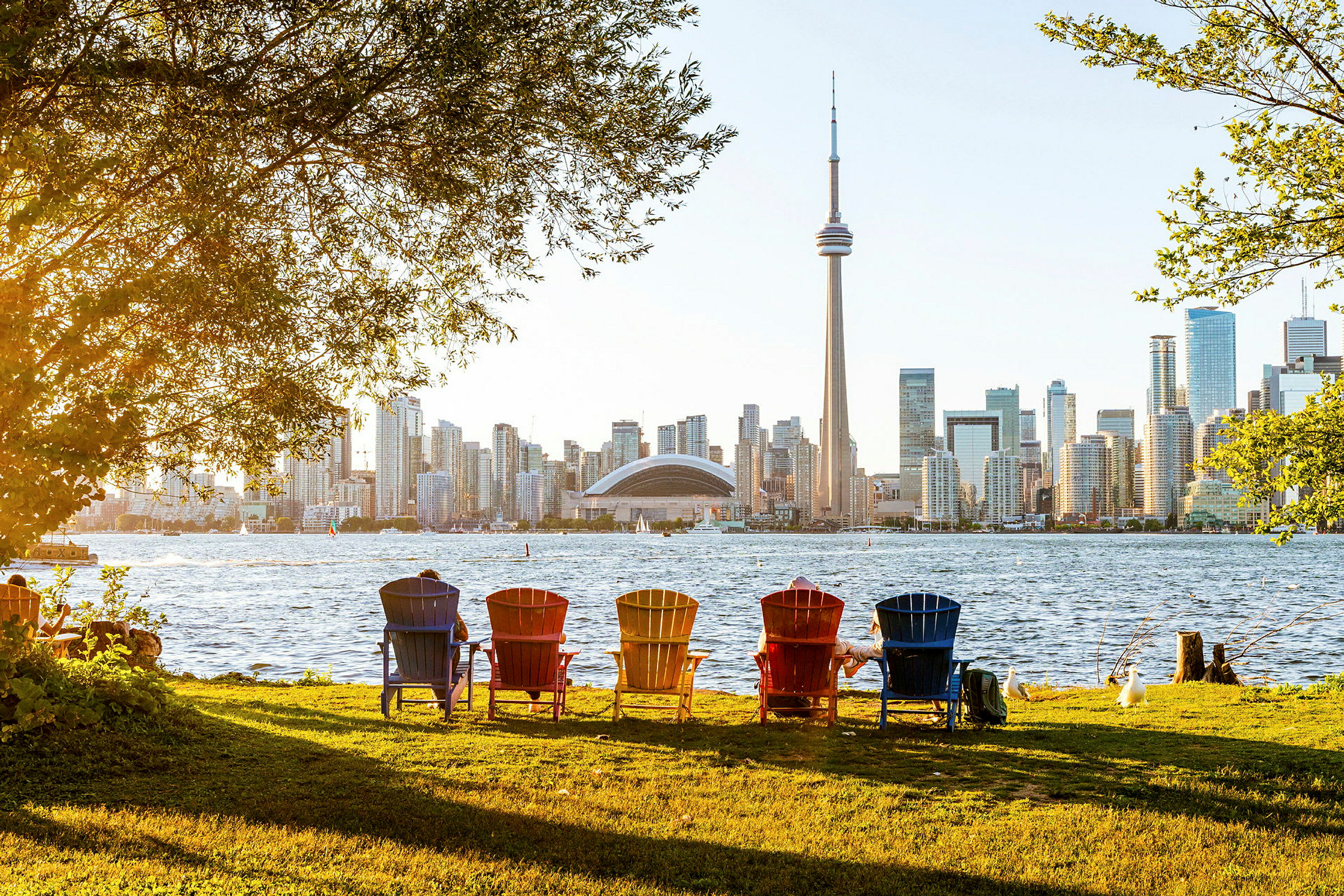 Fargede stoler i en park med utsikt mot en bysilhuett og CN Tower. (AI-generert tekst)