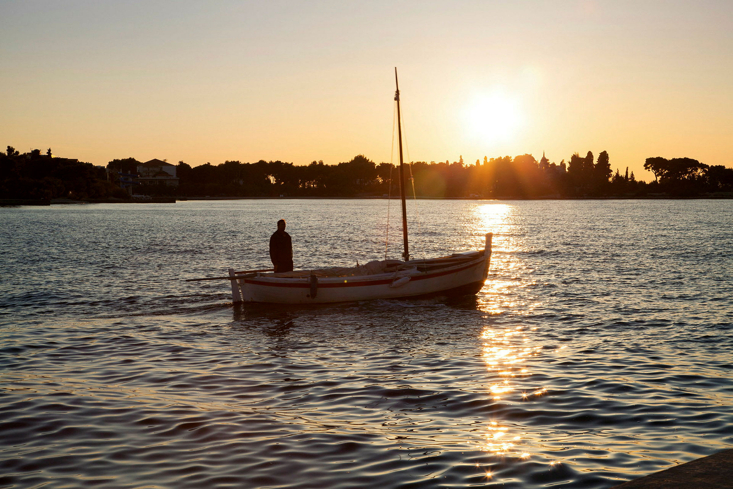 Mann står på liten båt i vann ved solnedgang. (AI-generert tekst)
