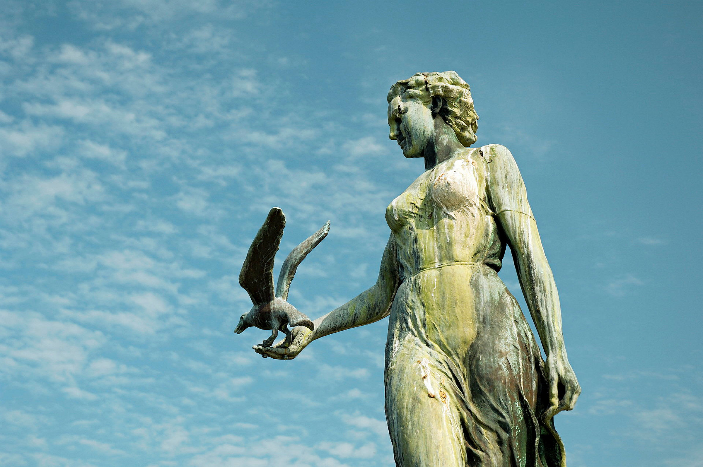 Statue av en kvinne med en fugl i hånden mot en blå himmel. (AI-generert tekst)