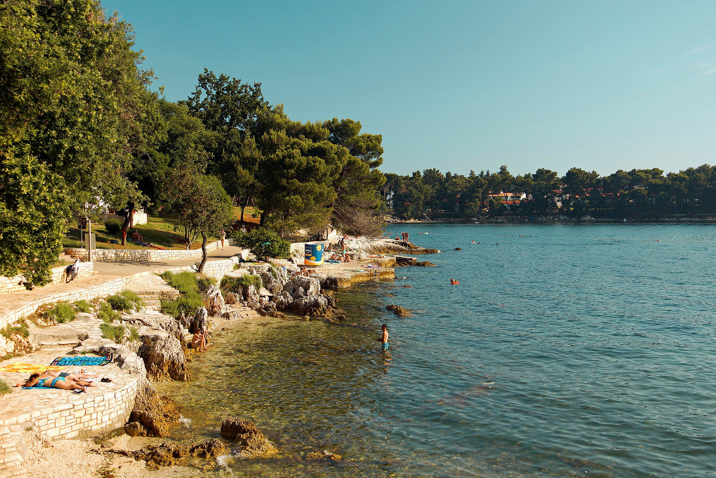 Kystlinje ved havet med mennesker som soler seg og bader. (AI-generert tekst)
