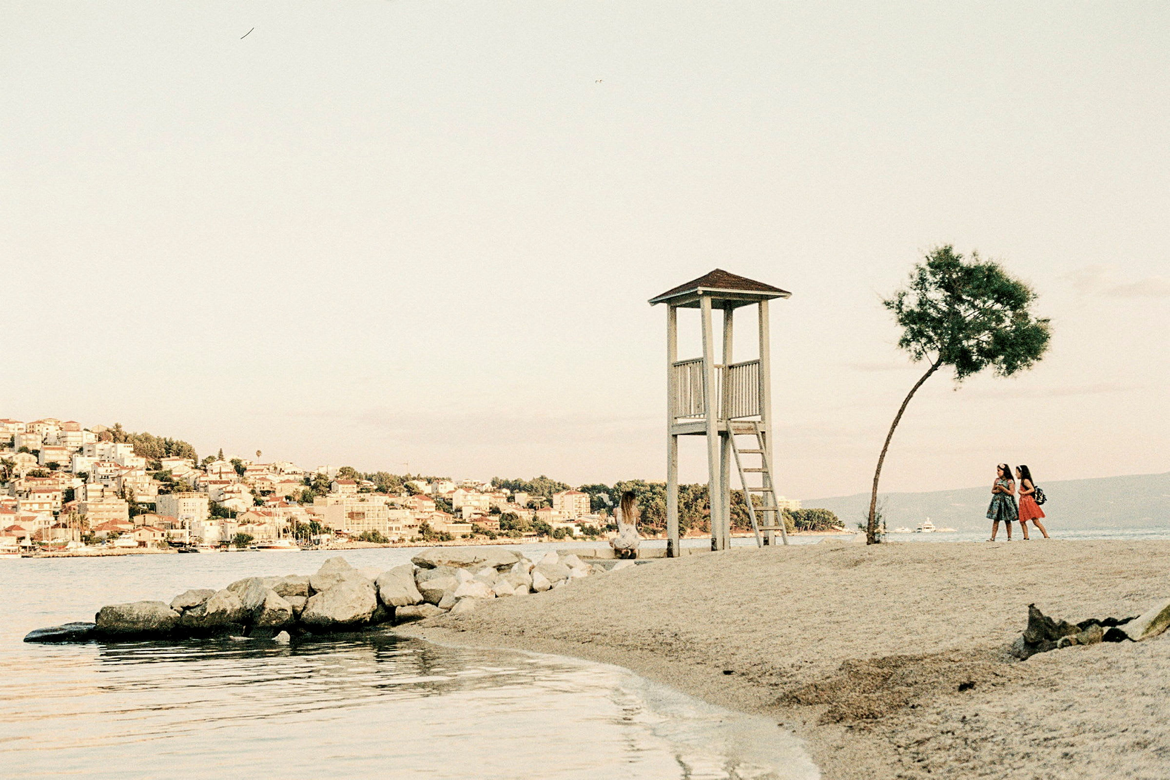 Vaktkur på en strand med to personer som går nær et tre. (AI-generert tekst)