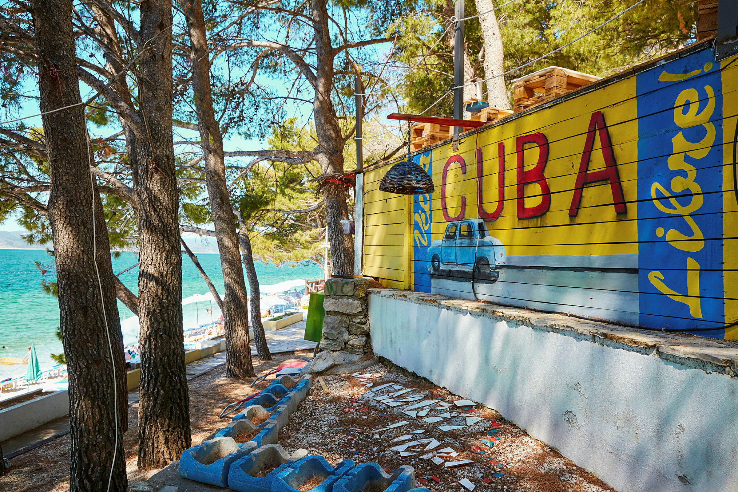 Veggmaling med teksten 'Cuba' og en blå bil i tropisk miljø. (AI-generert tekst)