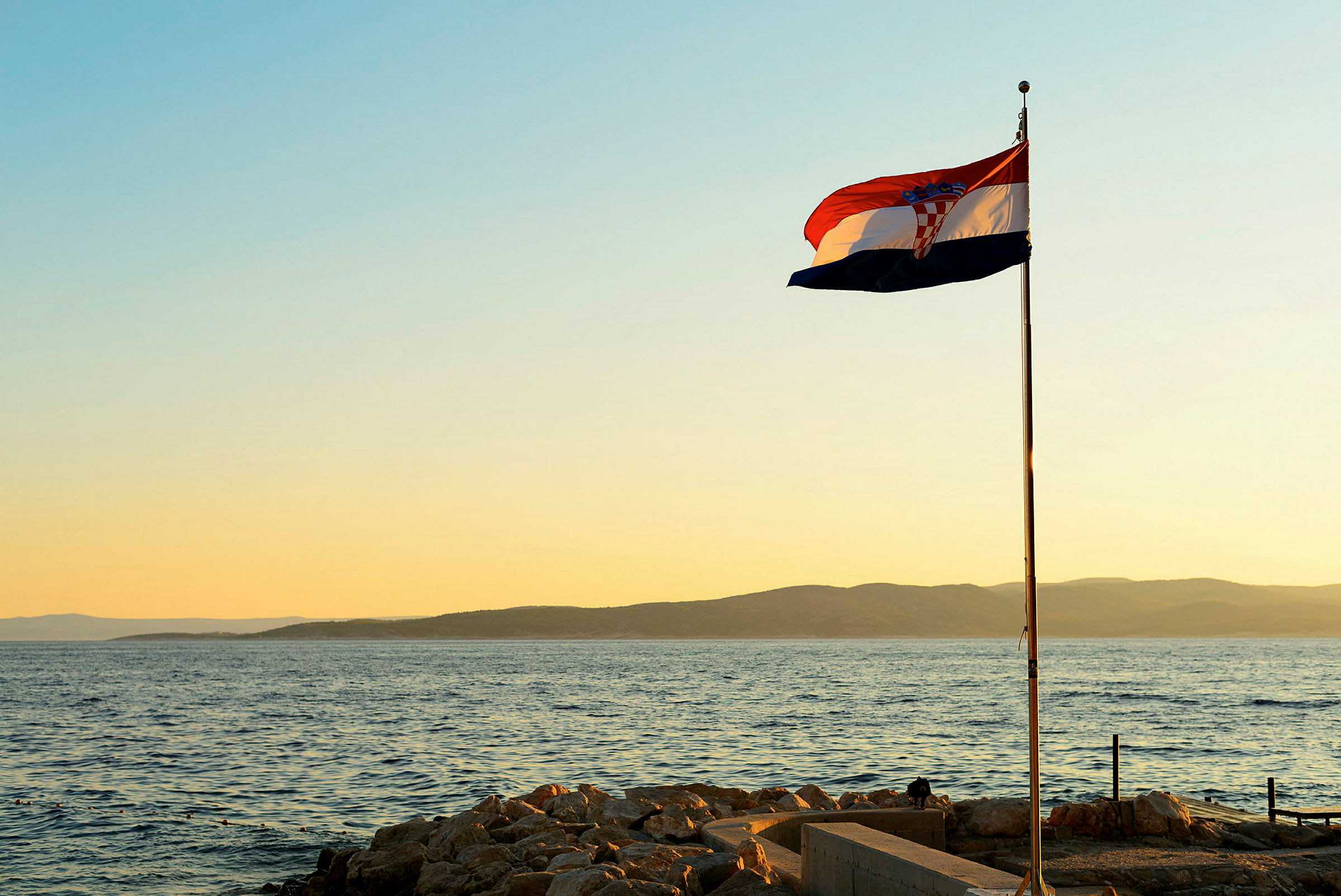 Det kroatiske flagget vaier ved kysten under solnedgangen. (AI-generert tekst)
