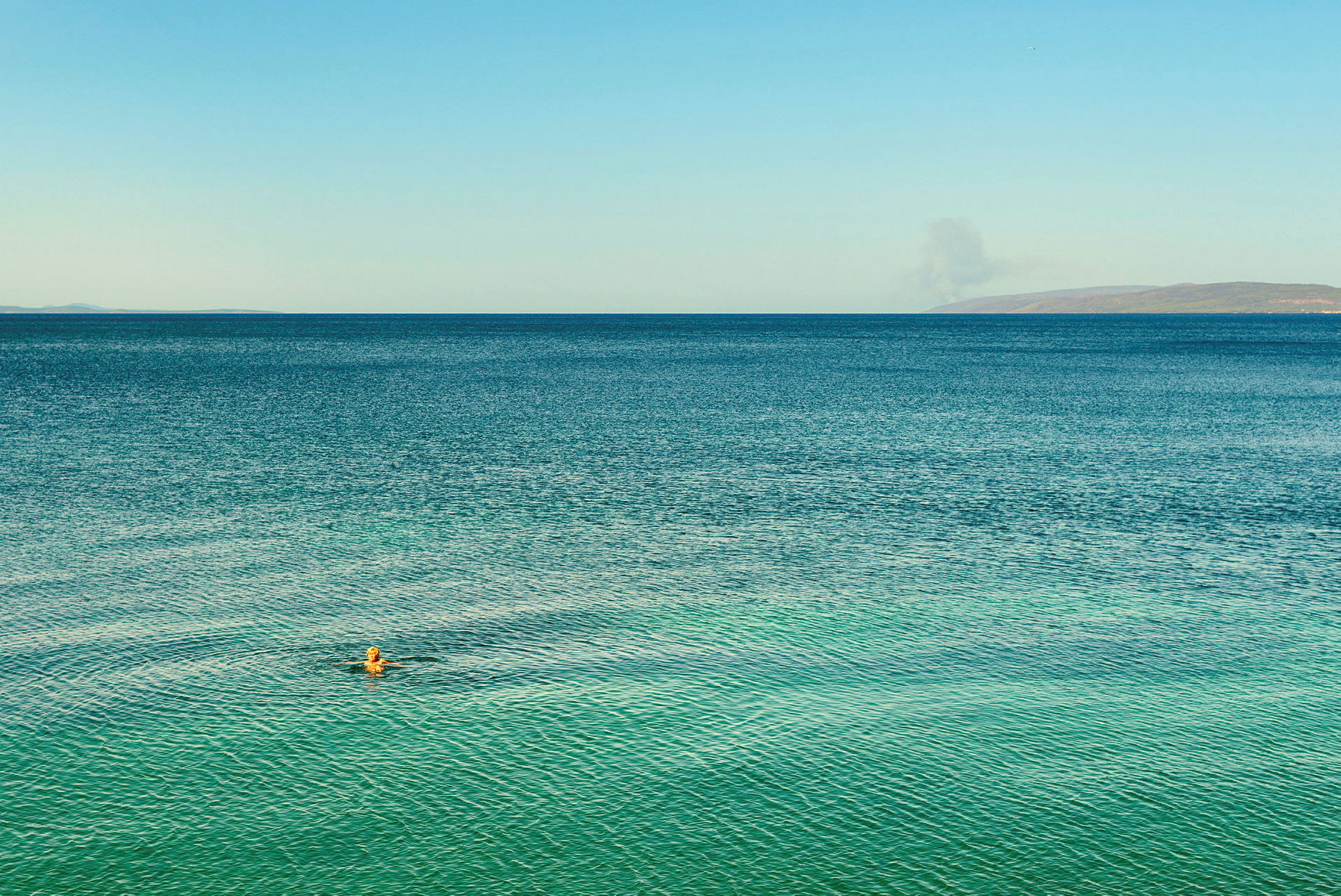 Person svømmer i havet under blå himmel. (AI-generert tekst)