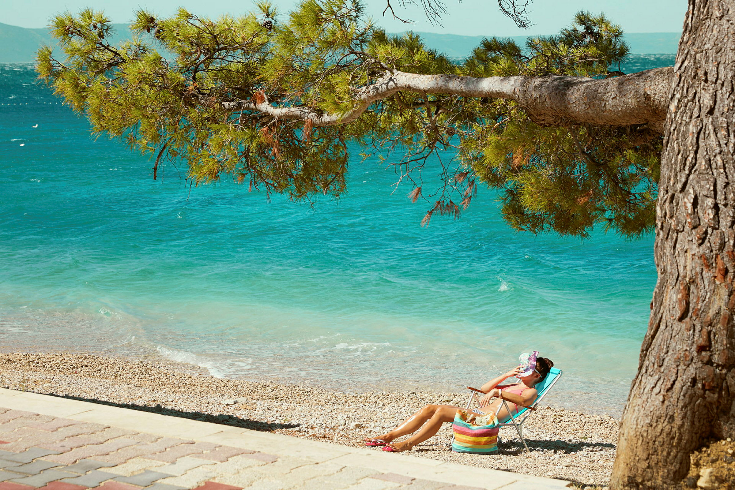 En person sitter i en solstol på en steinstrand med havet i bakgrunnen. (AI-generert tekst)