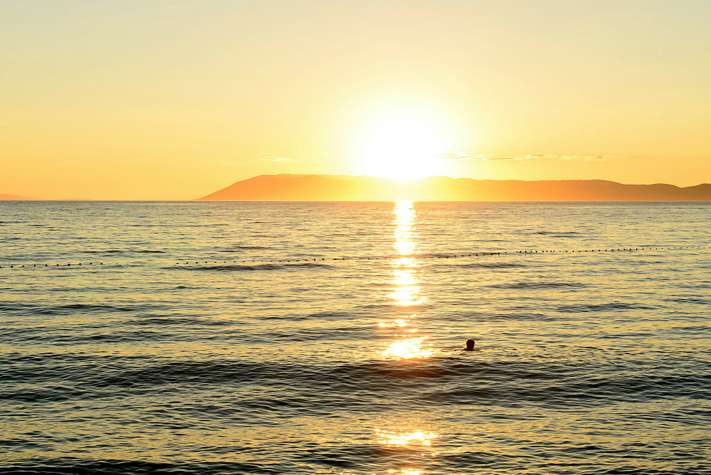 Solnedgang over havet med en silhuett av en svømmende person. (AI-generert tekst)