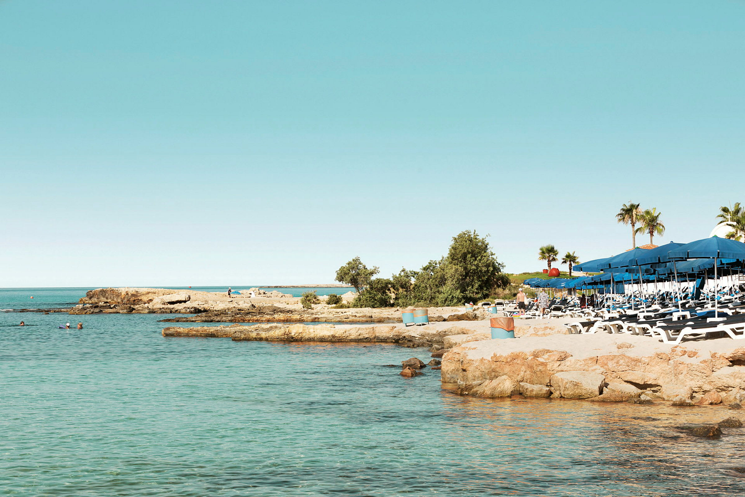 Bilde av en strand med solsenger og parasoller ved siden av klart vann. (AI-generert tekst)