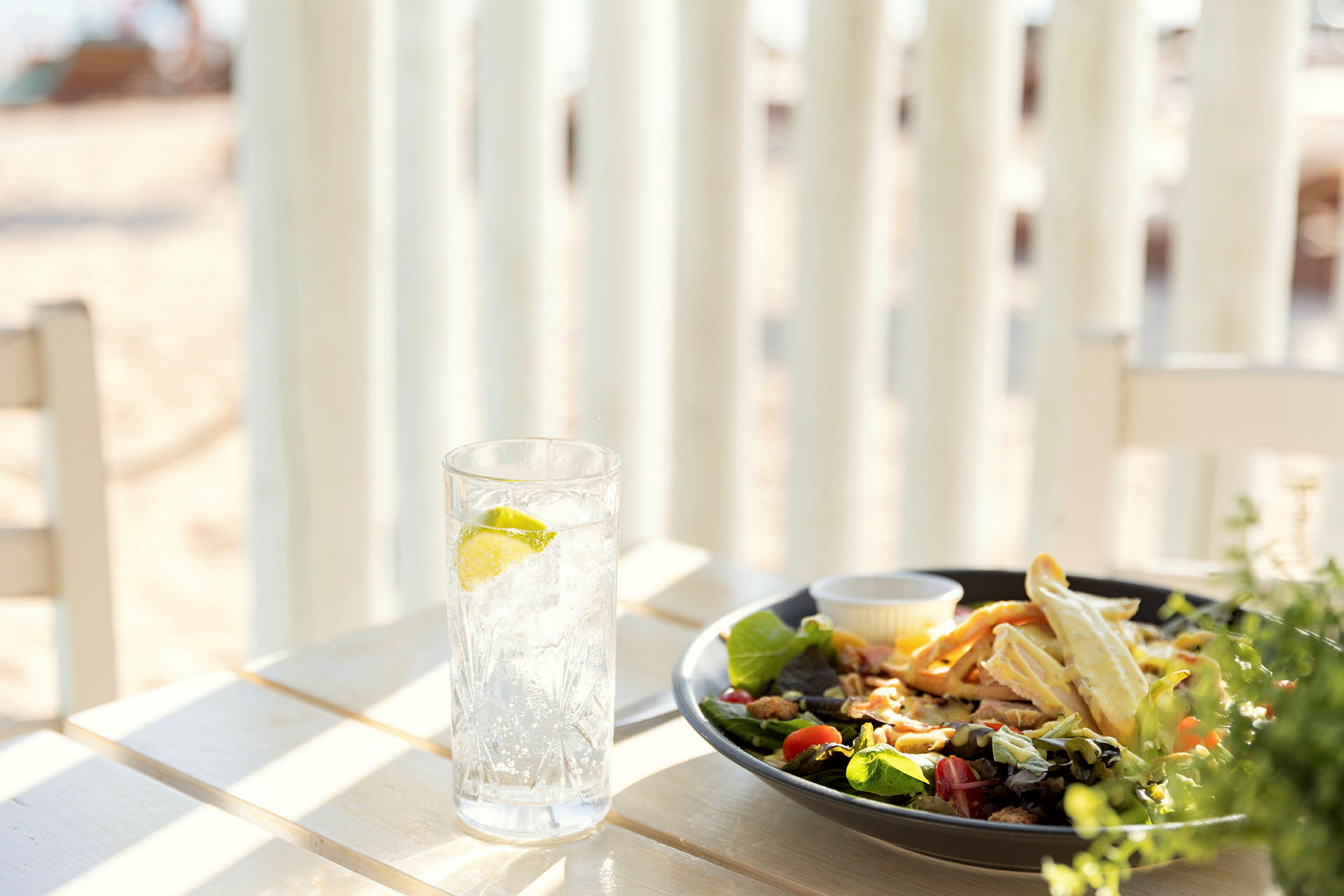 Et bord med et glass vann med lime og en tallerken salat ved stranden. (AI-generert tekst)