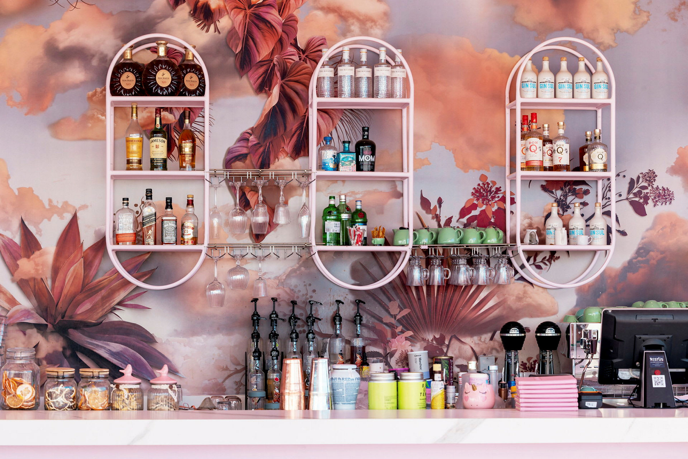 En bar med rosa hyller fylt med spritflasker, glass og dekor med planter. (AI-generert tekst)