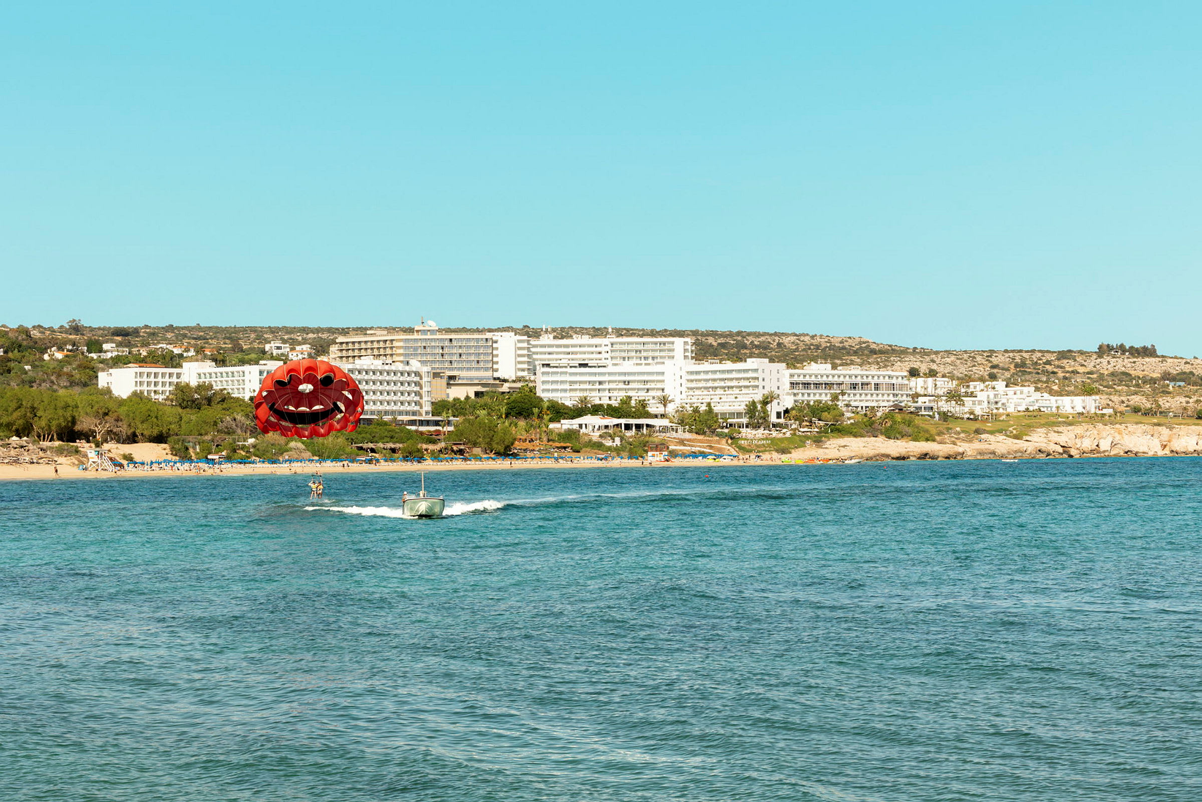 Bilde av en strand med et hotell i bakgrunnen og en person som driver med parasailing foran. (AI-generert tekst)