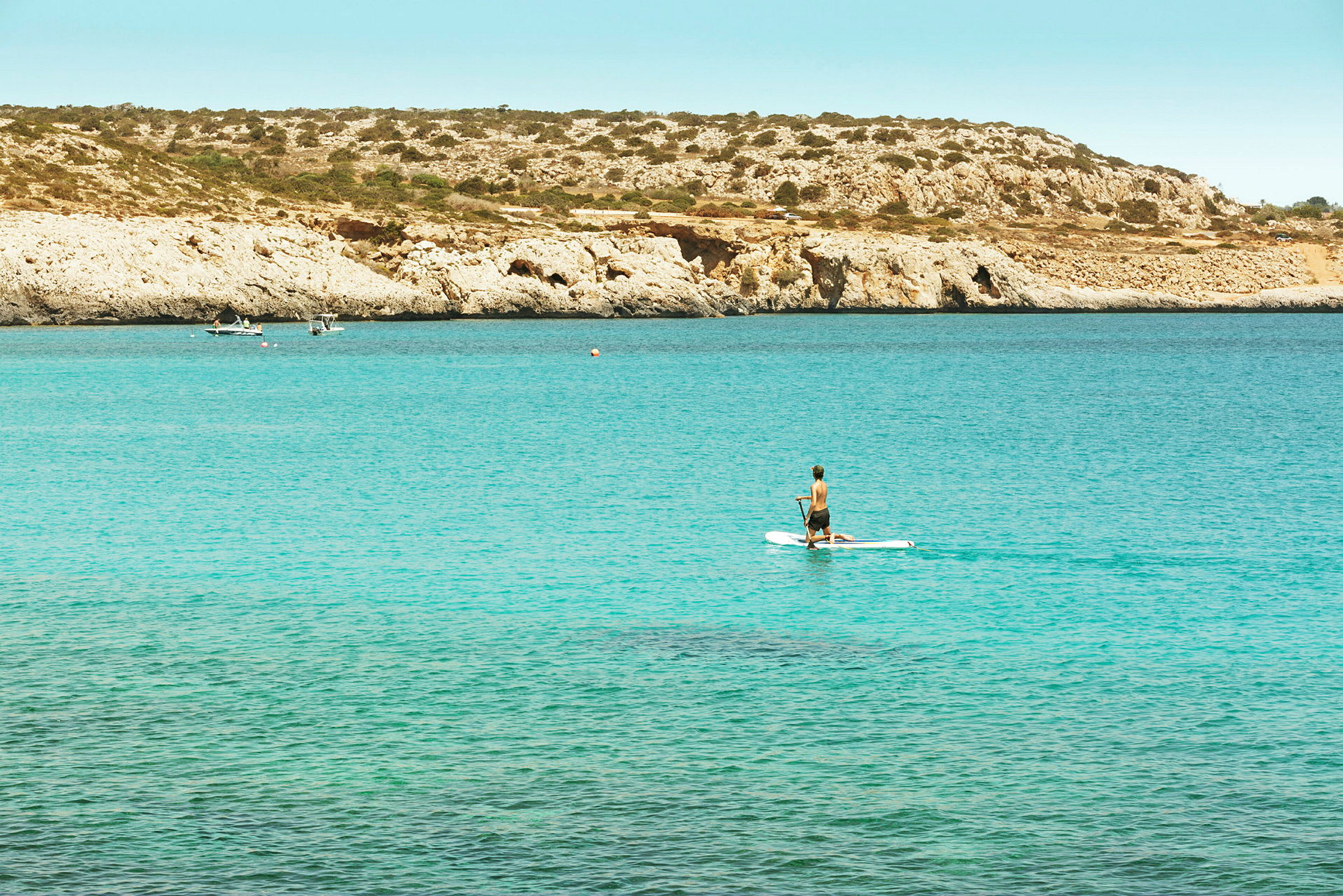 En person som padler på et paddleboard med klipper og hav i bakgrunnen. (AI-generert tekst)