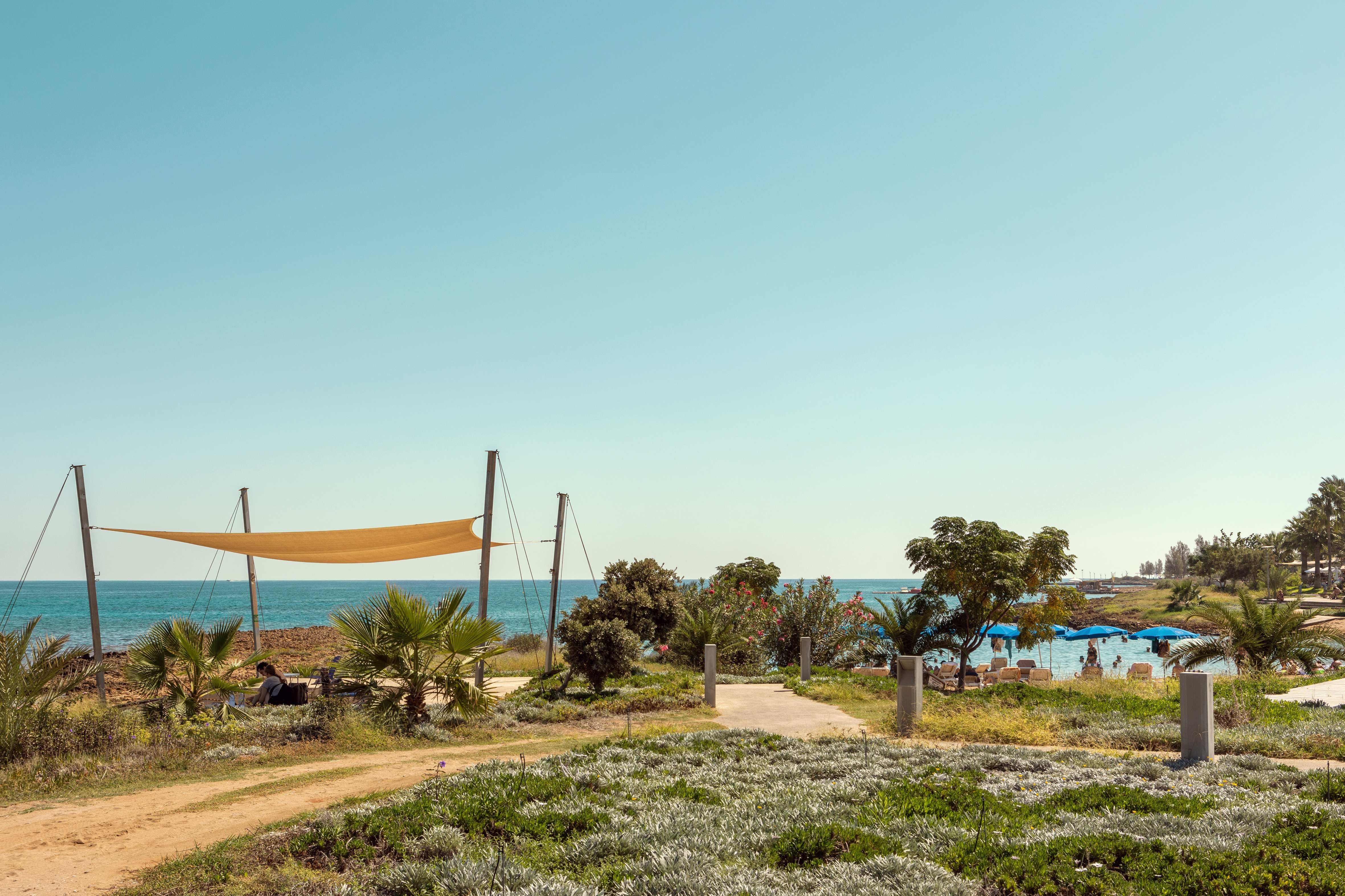 Utsikt mot stranden med blå parasoller og grøntområder. (AI-generert tekst)