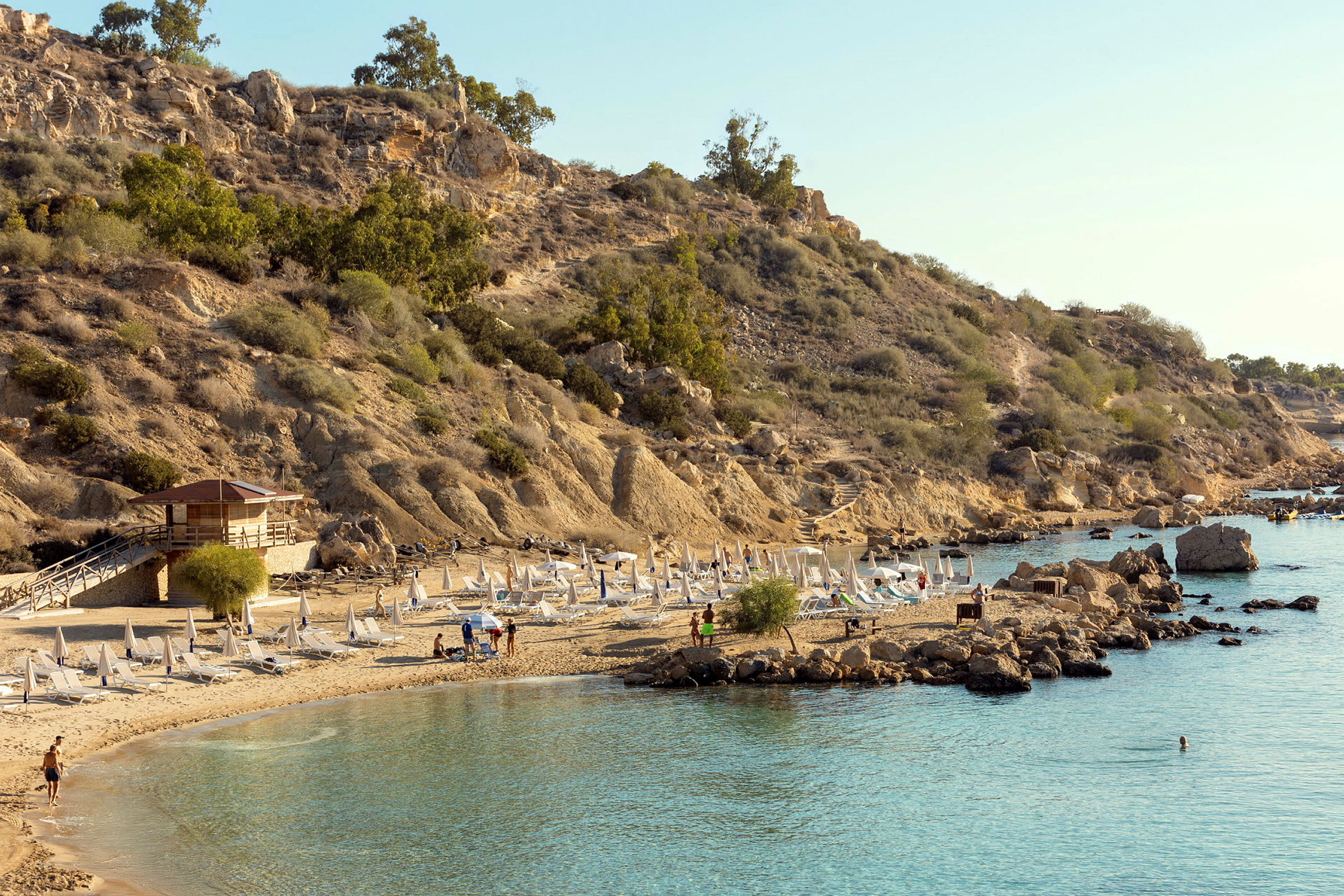 En klippekyst med solsenger og parasoller på en sandstrand. (AI-generert tekst)