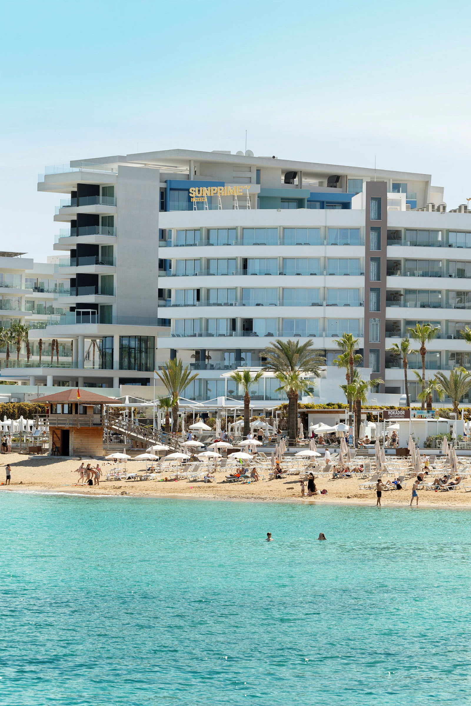 Et strandhotell med solsenger og turkis hav i forgrunnen. (AI-generert tekst)