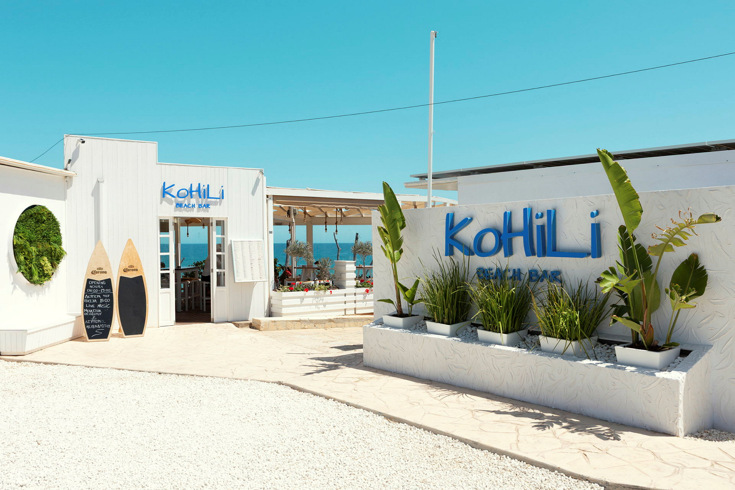 Inngang til Kohili Beach Bar med dekorative planter og en klar blå himmel. (AI-generert tekst)