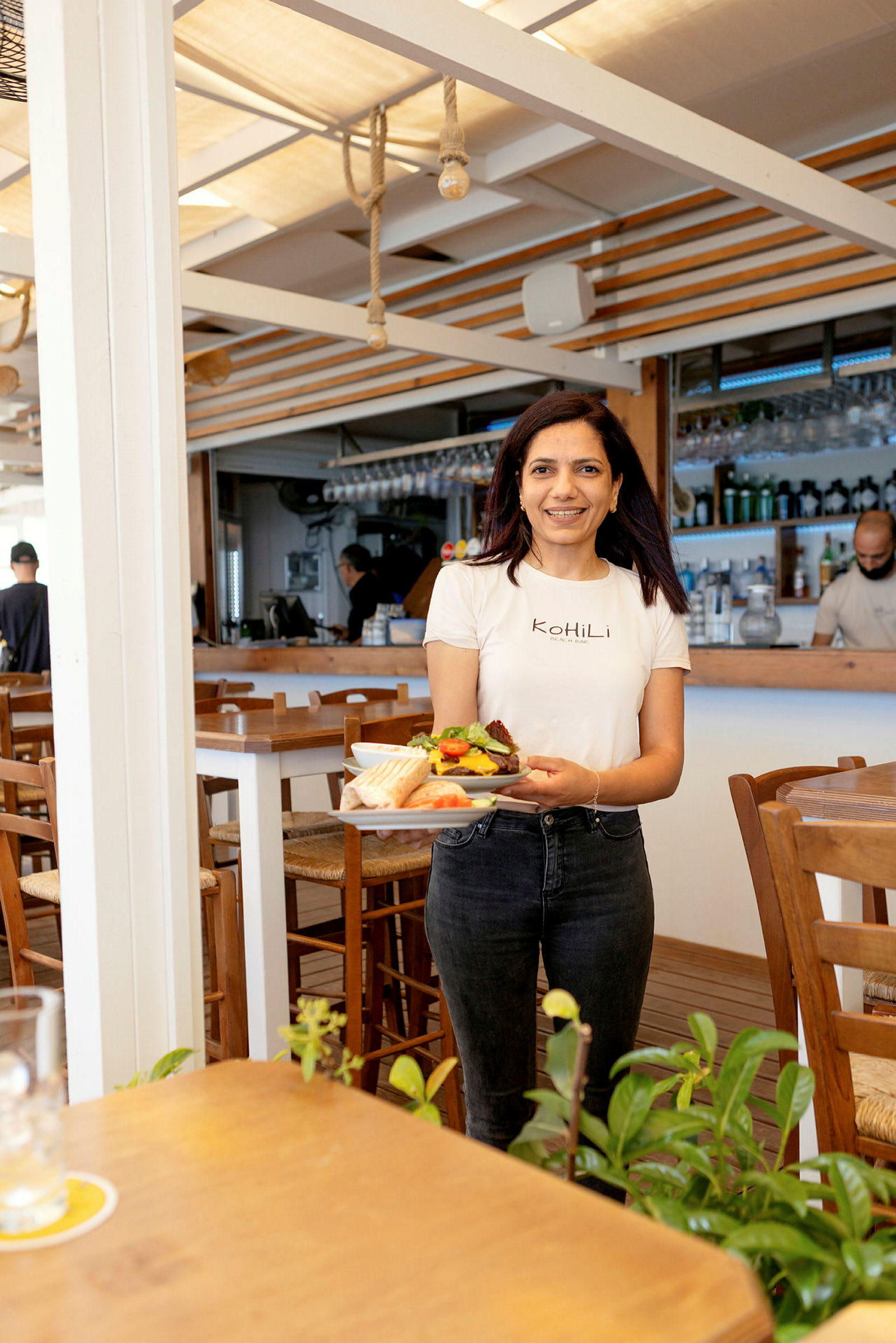 En person holder en tallerken med mat i en restaurant med treinteriør og planter i forgrunnen. (AI-generert tekst)