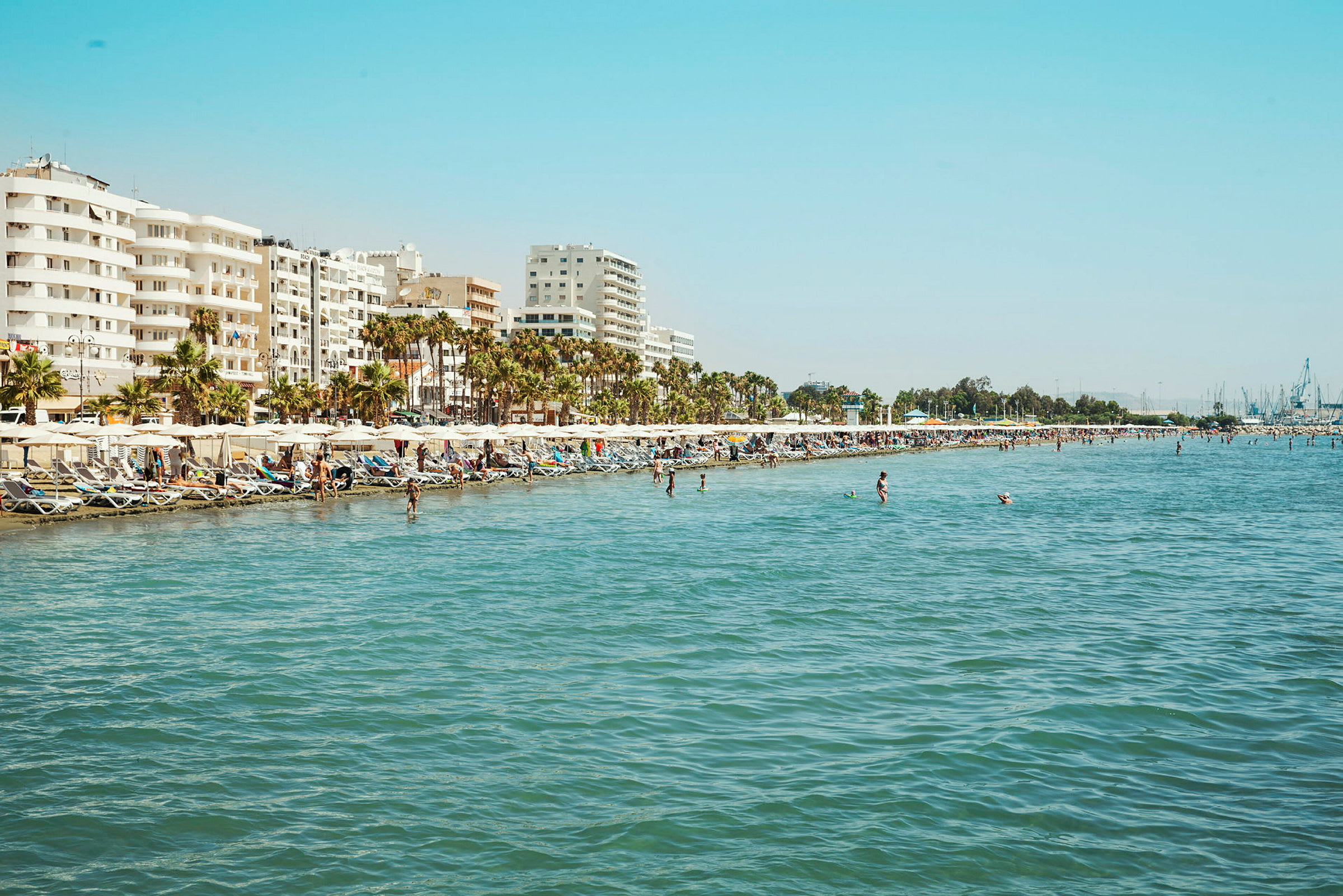 Strand med solsenger og parasoller, ved en by med fleretasjes bygninger. (AI-generert tekst)