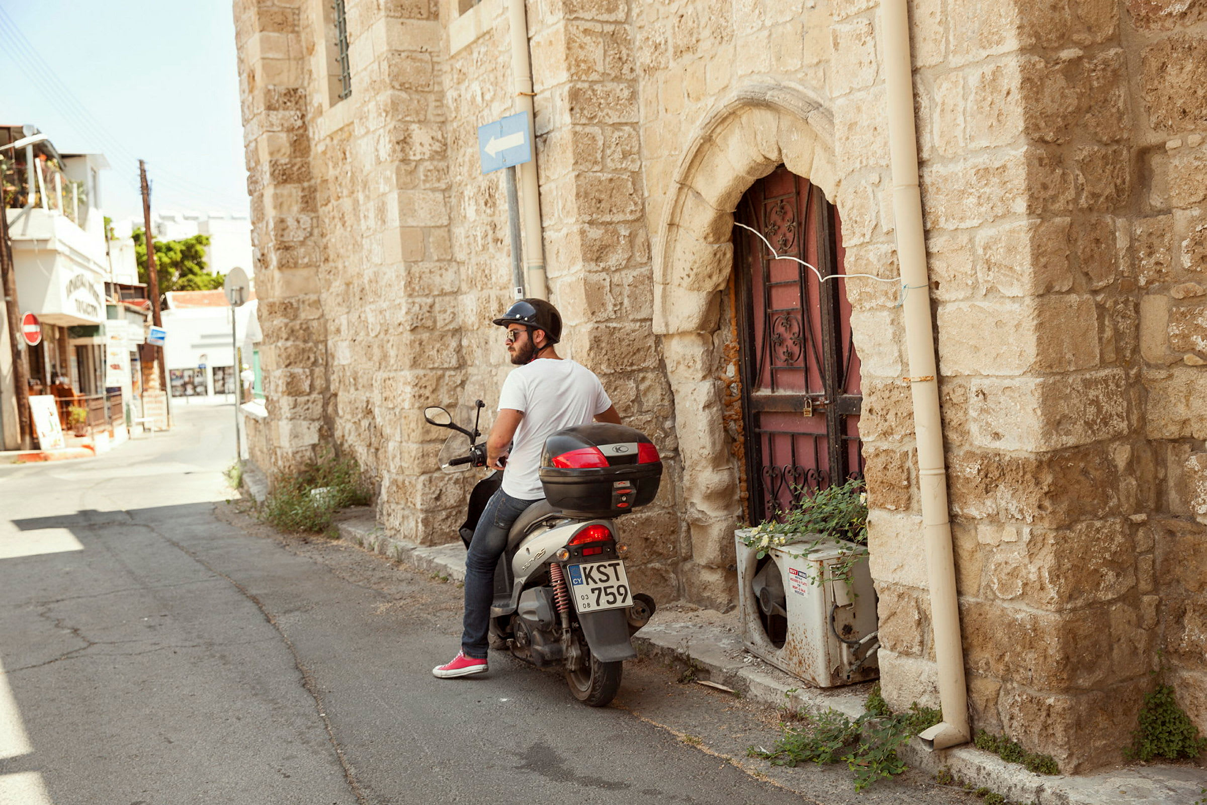 En mann sitter på en moped ved en steinbygning med en dekorert dør. (AI-generert tekst)