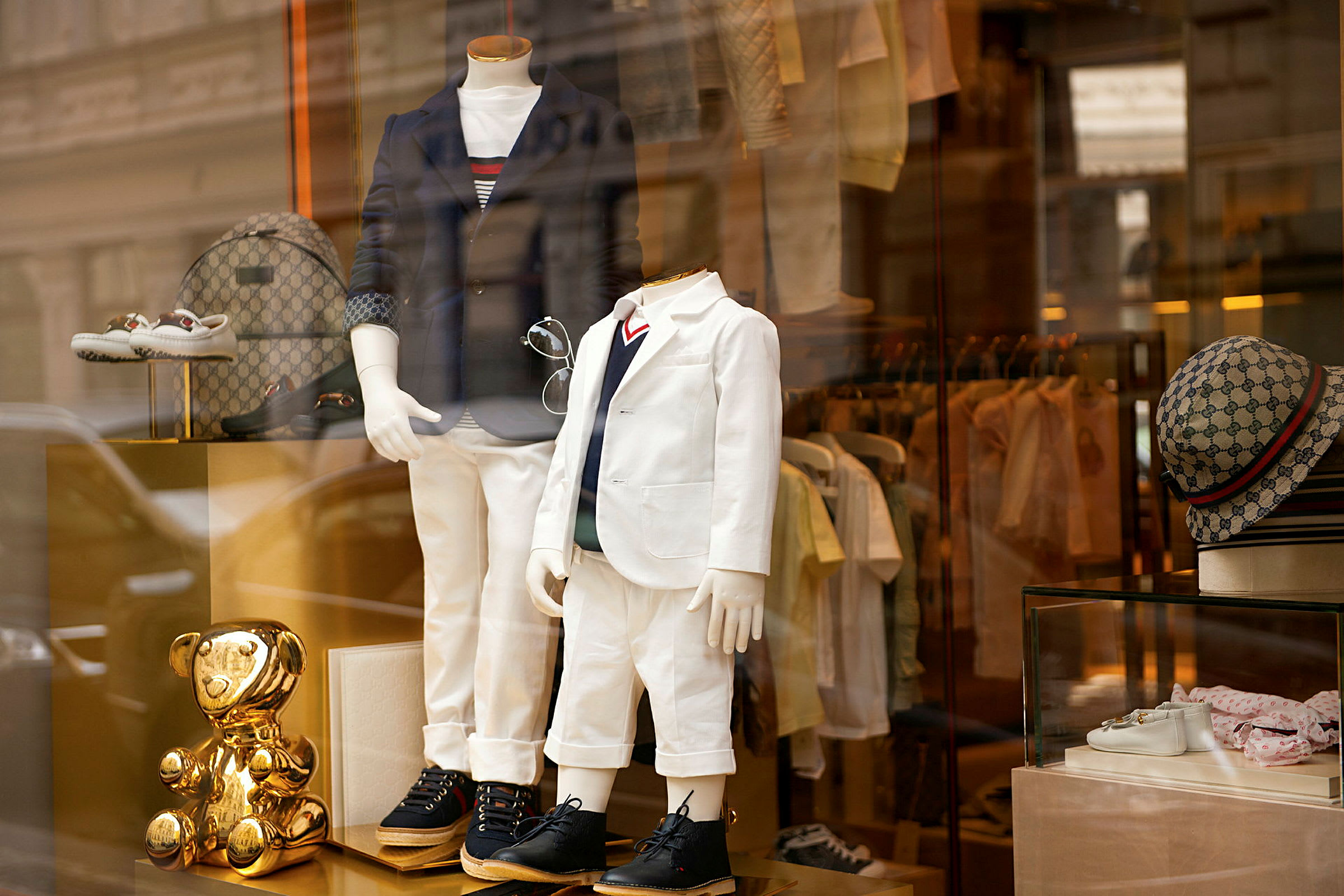 Butikkvindu med to mannequindukker kledd i elegante antrekk, omgitt av tilbehør og et gyllent pynteobjekt. (AI-generert tekst)