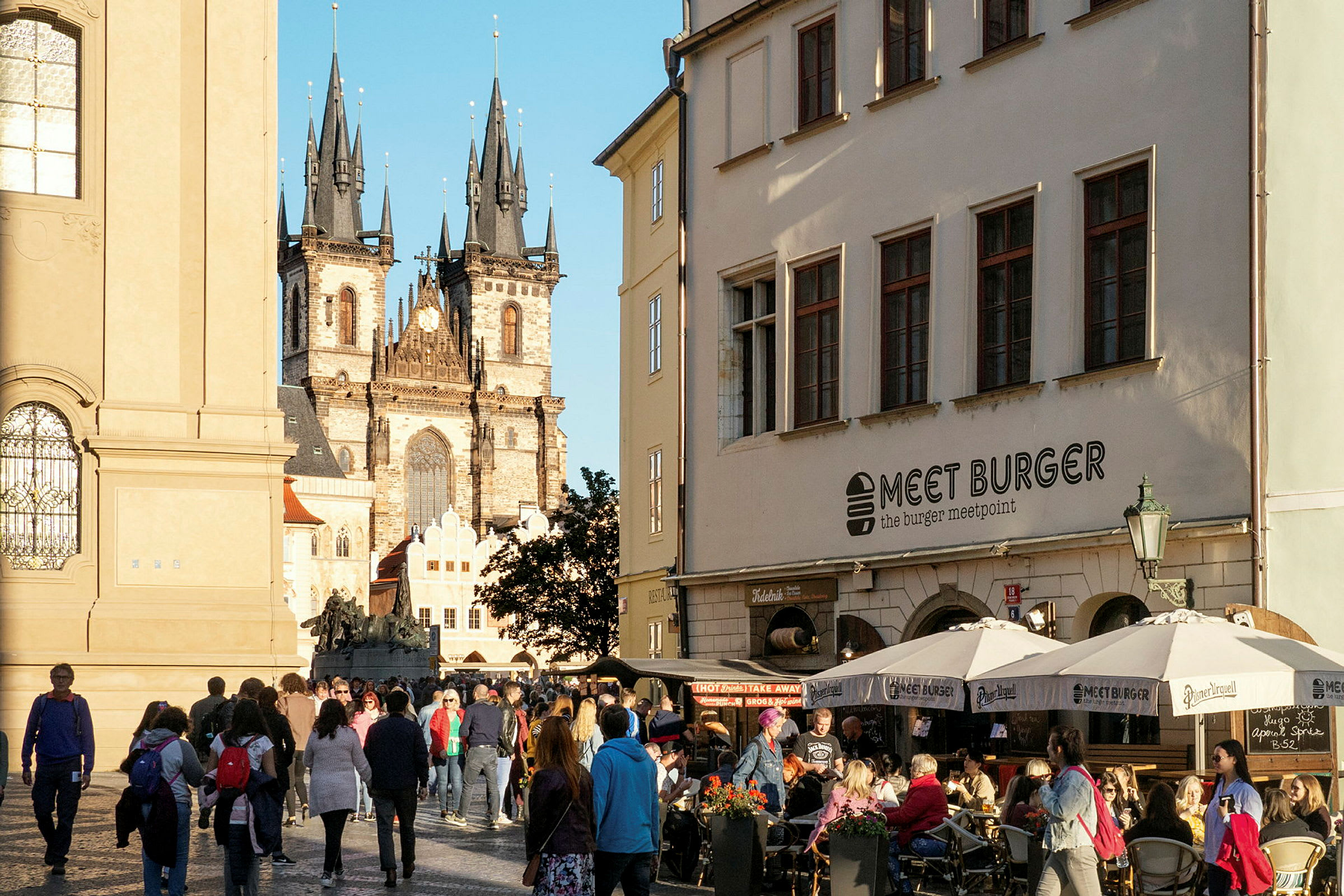Bilde av en travel bygate med en kaféutservering i forgrunnen og en historisk gotisk kirke i bakgrunnen. (AI-generert tekst)
