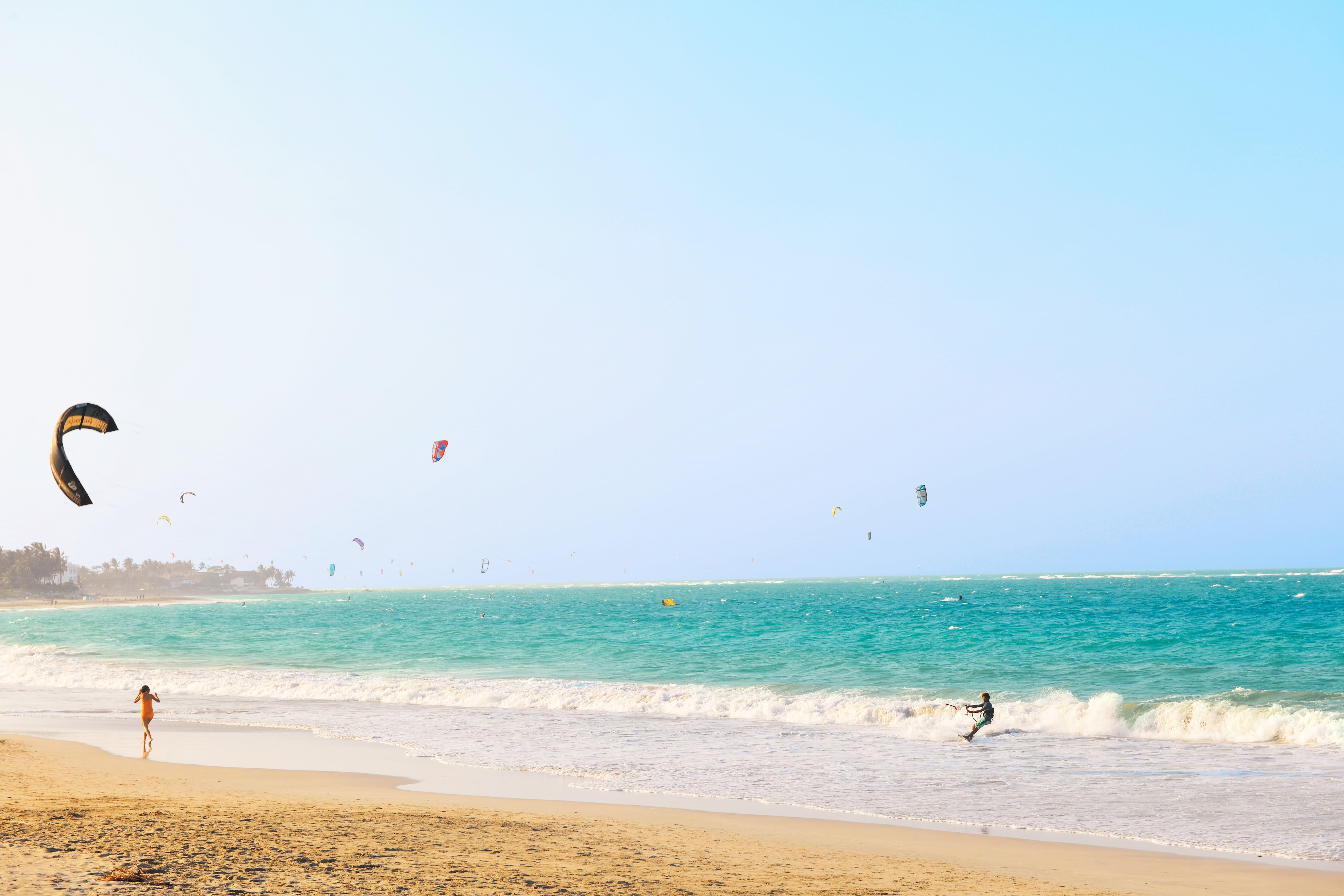 En strand med turkist hav og mange kitesurfere. (AI-generert tekst)