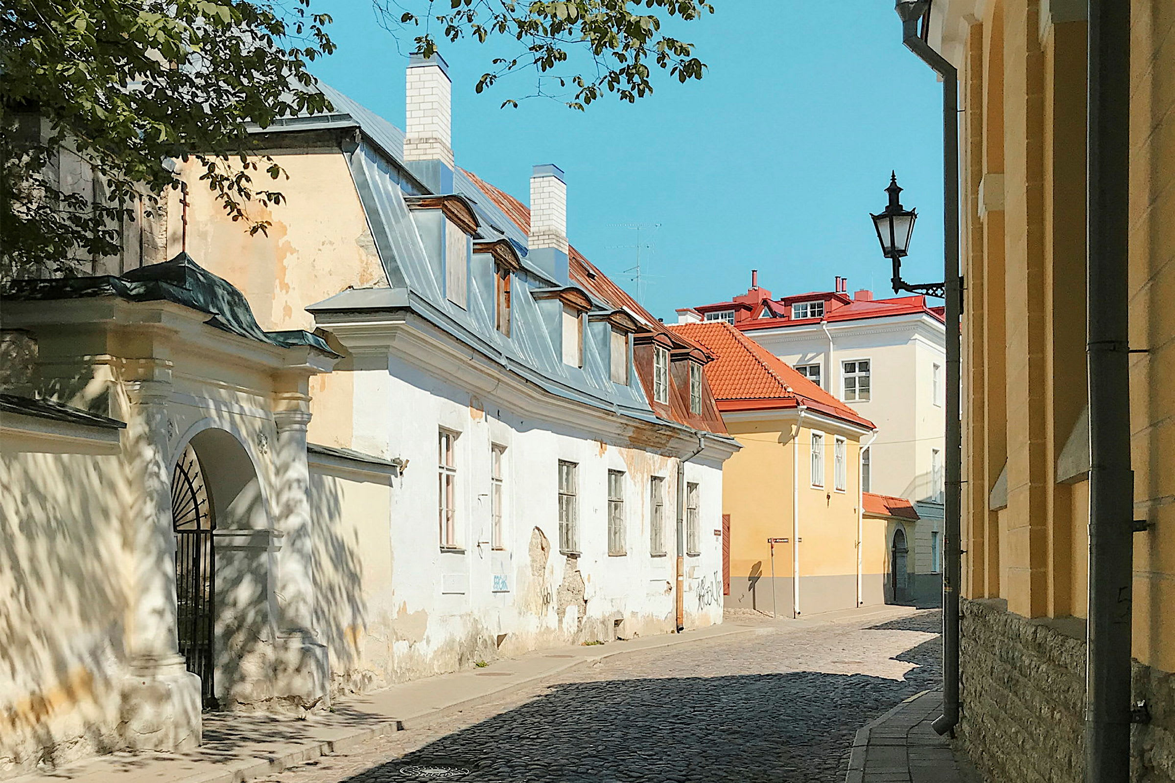 En smal gate omgitt av gamle bygninger med tegl- og blikkbelagte tak under en klarblå himmel. (AI-generert tekst)